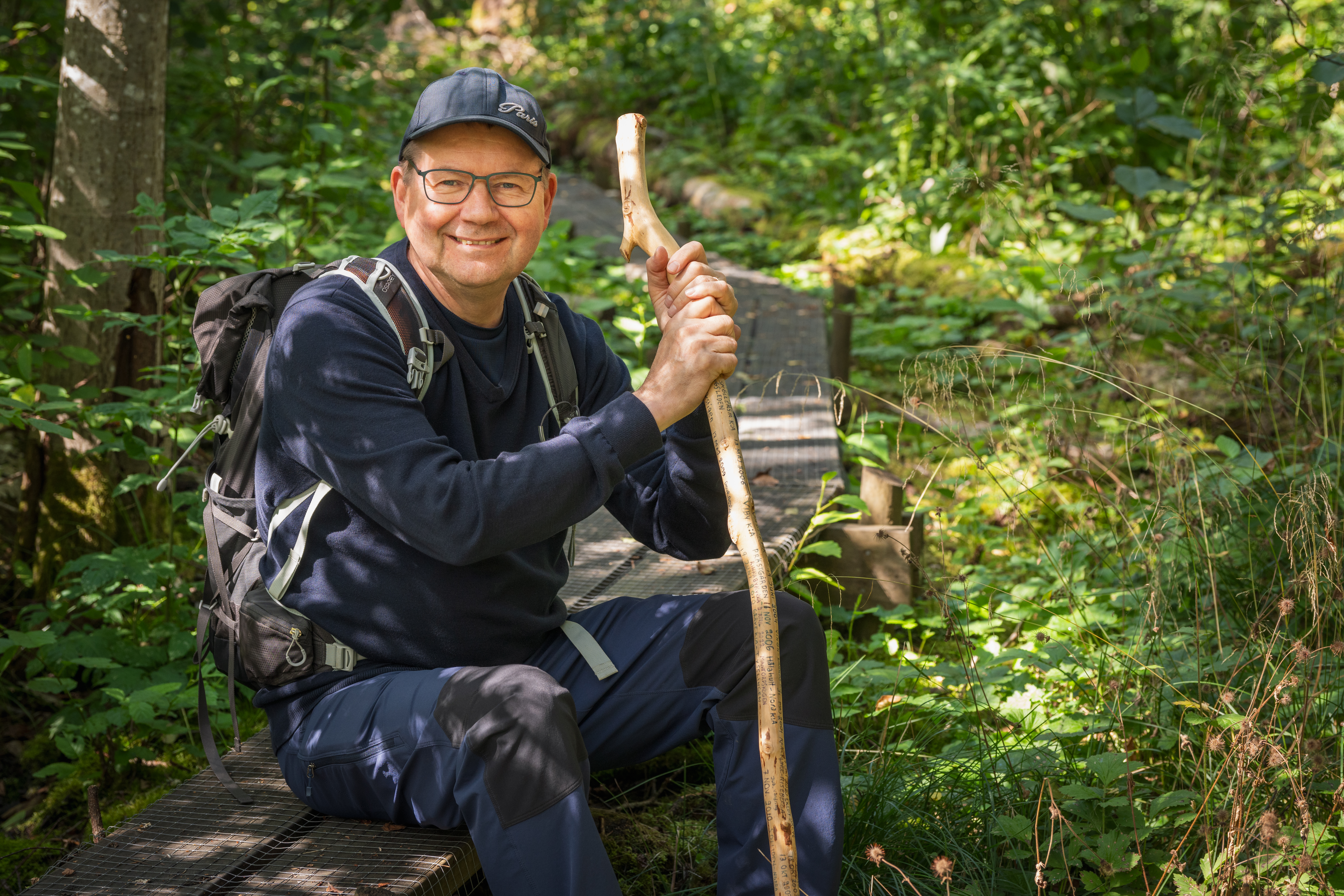 En man sitter i skogen med en vandringsstav.