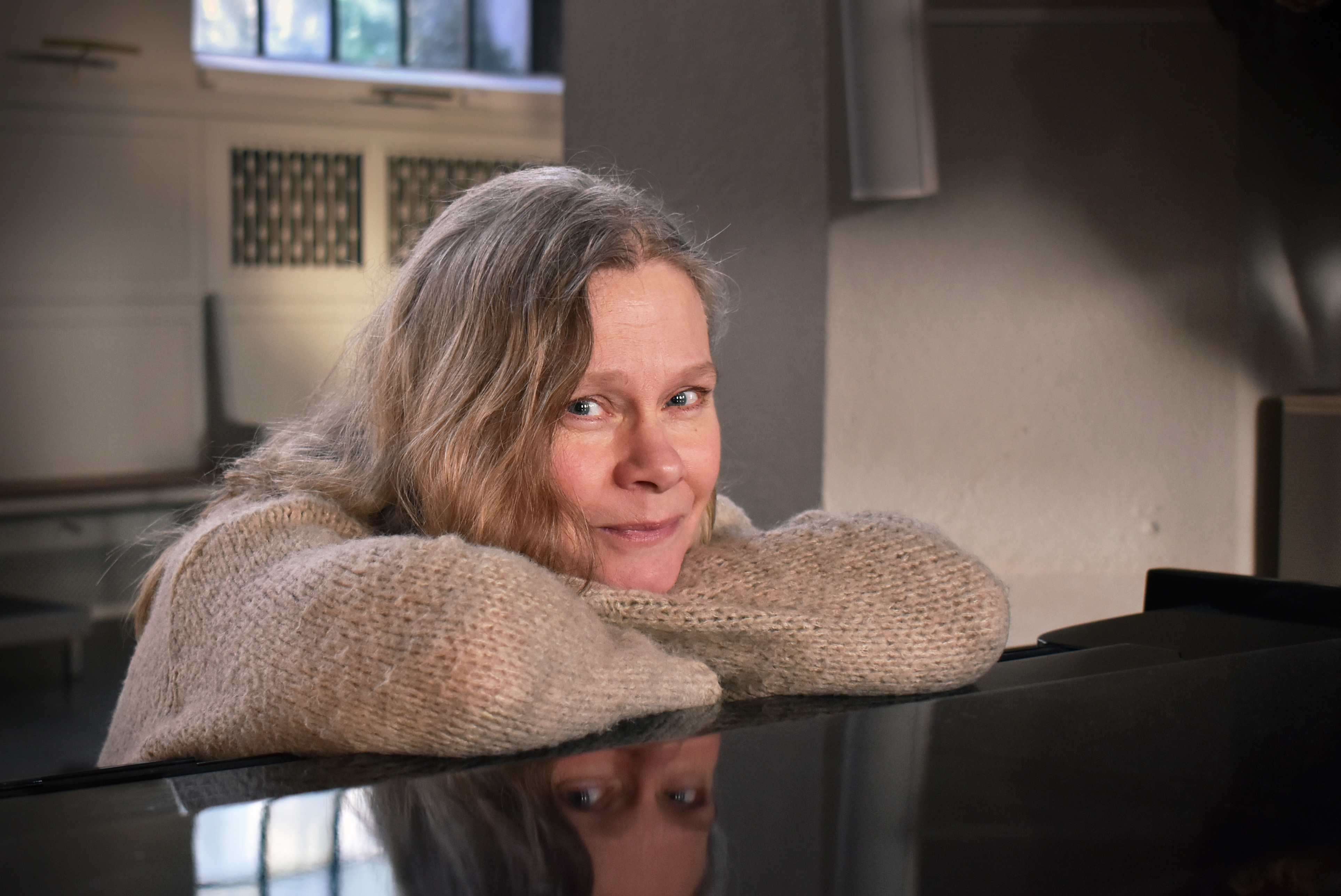 Kvinna i ylletröja hänger på locket till en flygel.