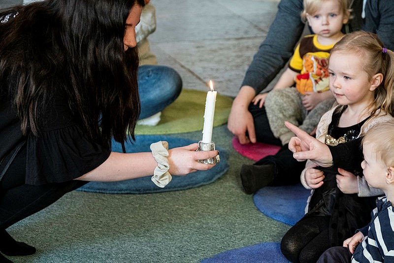 En kvinna visar ett ljus för en grupp barn som tittar nyfiket.