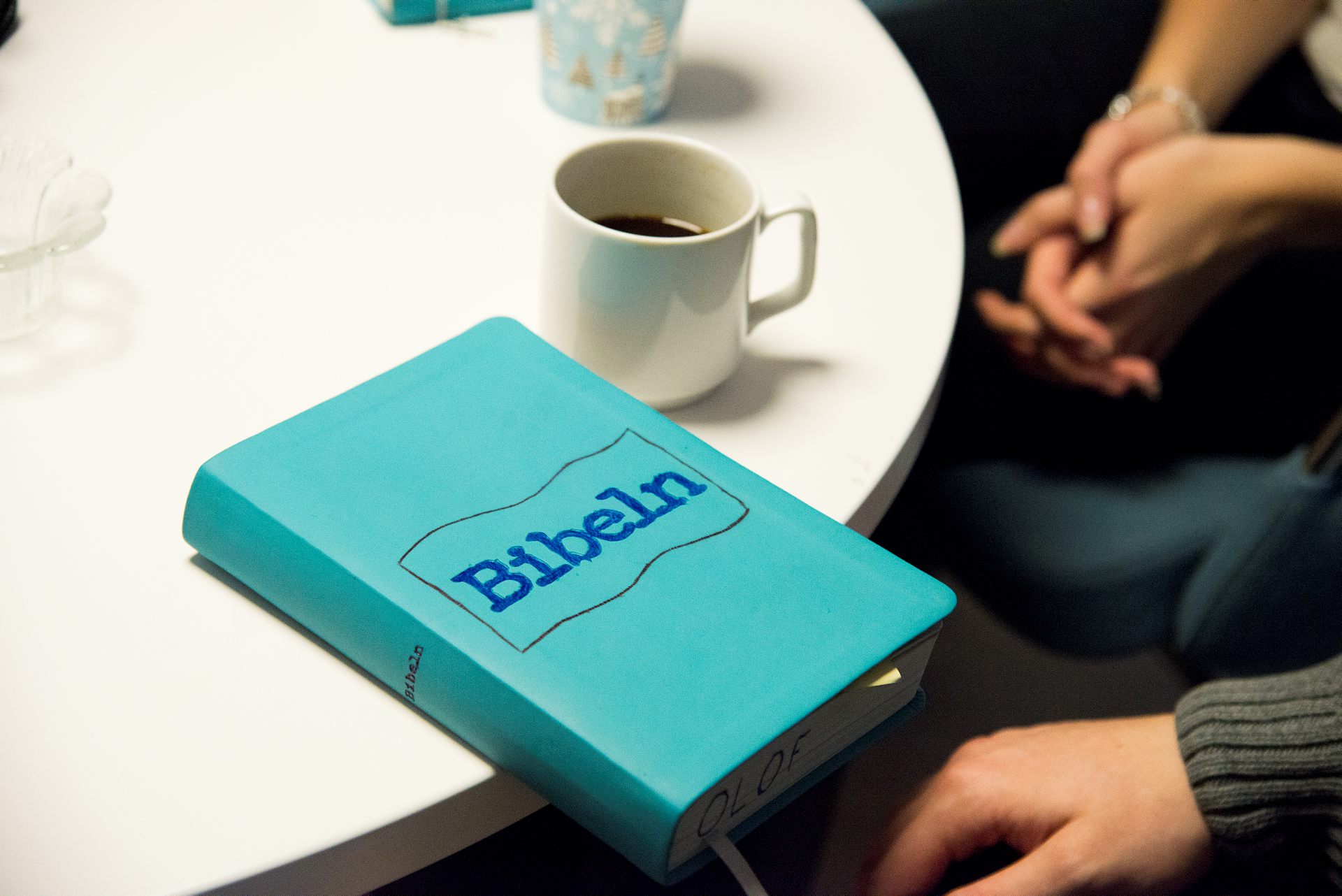 En bibel ligger på ett bord intill en kaffekopp.
