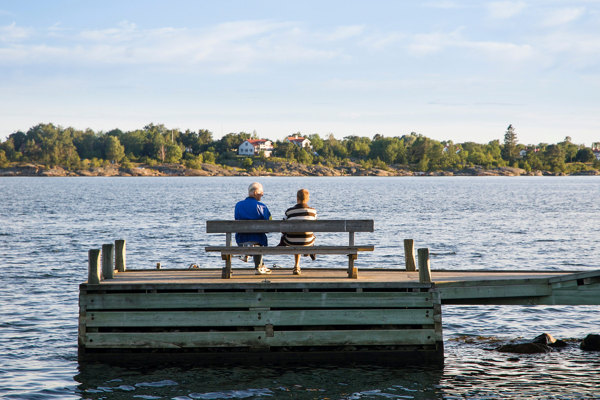 Sjö med brygga där det sitter en man och kvinna på en bänk