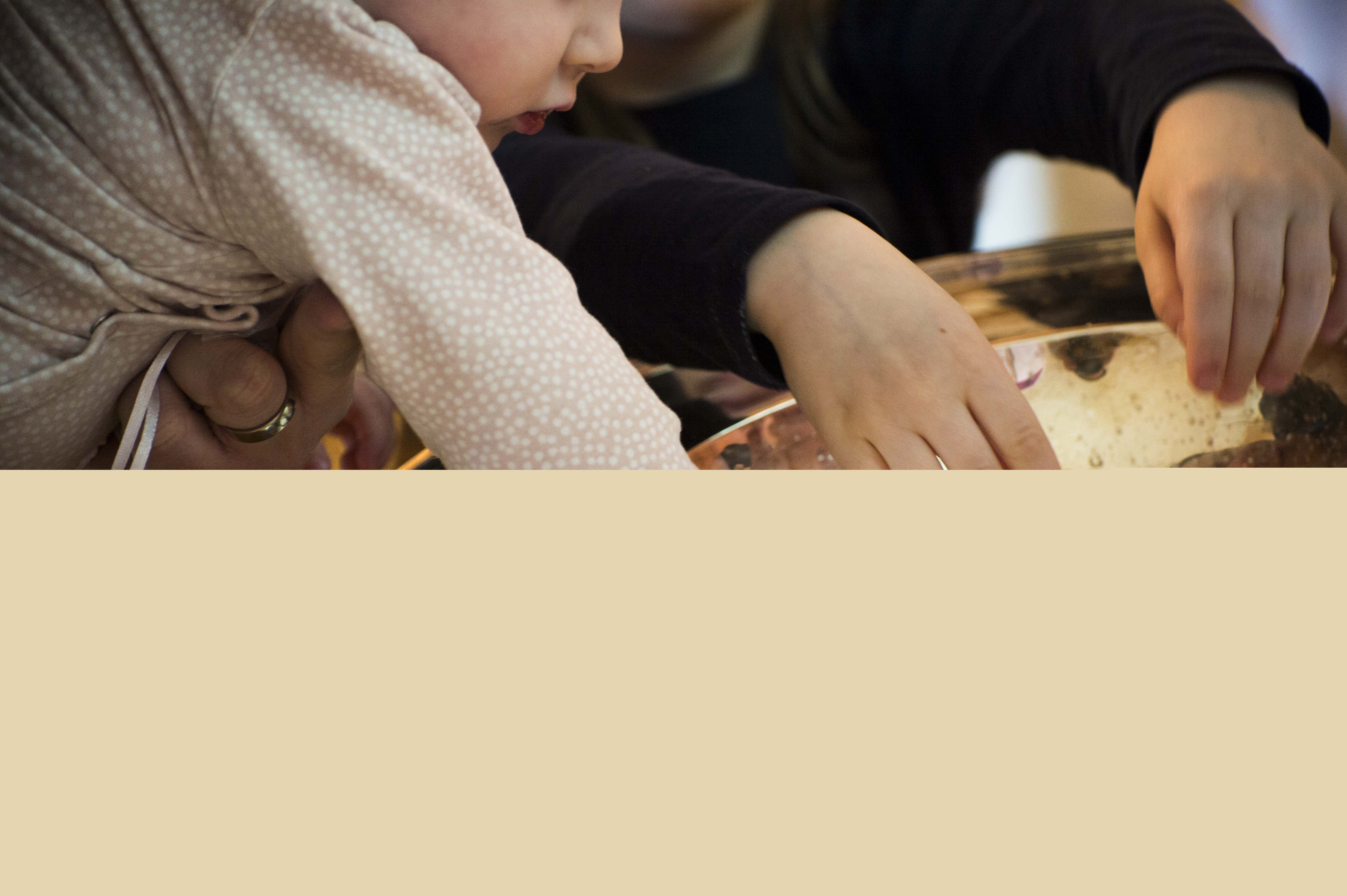 Närbild på dopfunt med barnhänder som rör vid vattnet i dopskålen