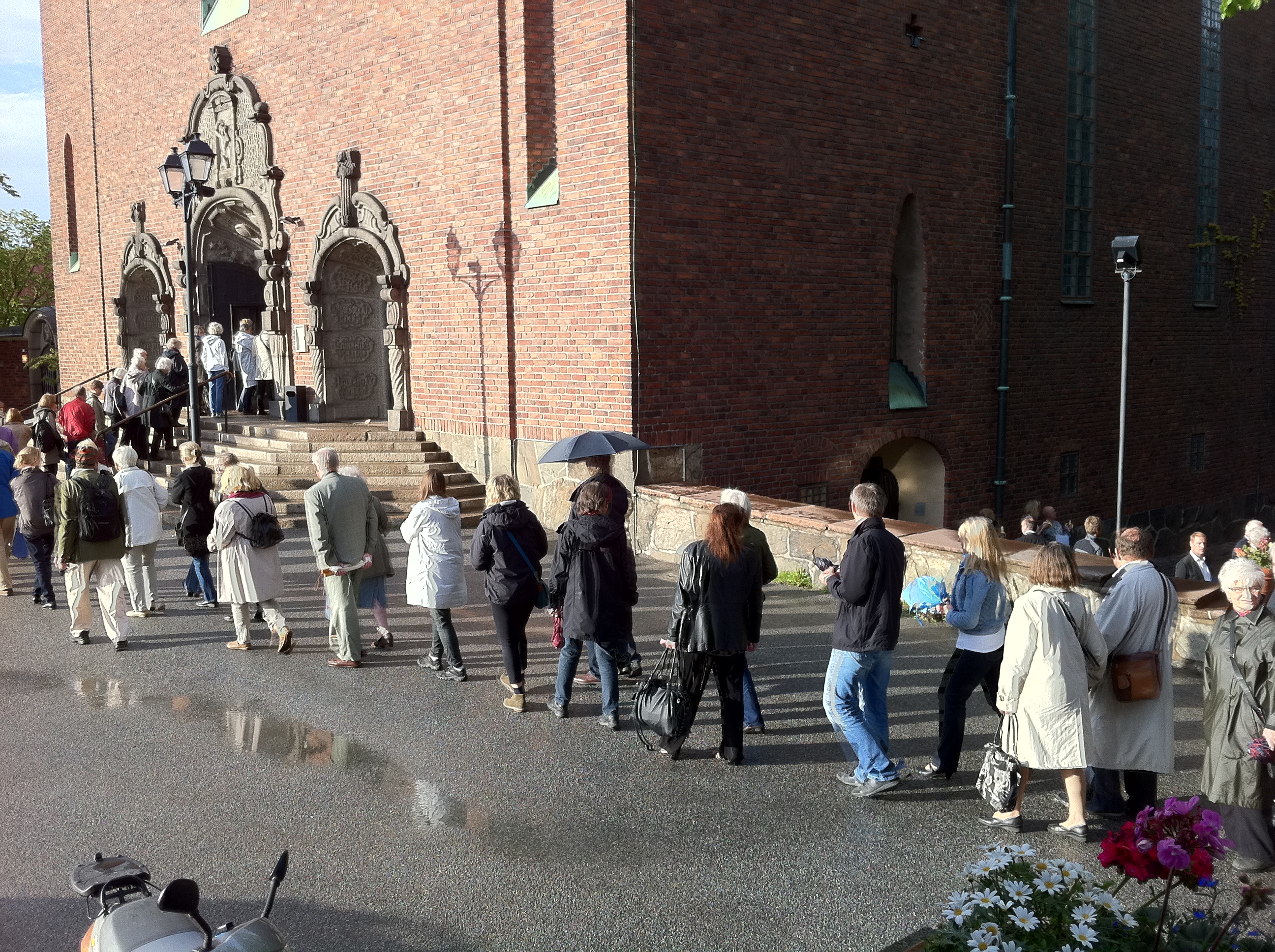 Ett stort antal människor i kö till till Högalidskyrkan. Det är blött på marken. 