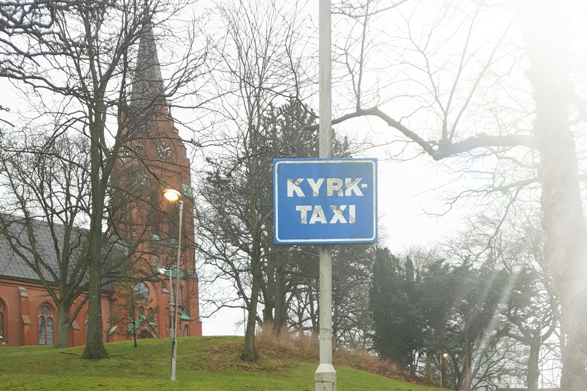 I bakgrunden syns Fässbergs kyrka. En skylt med "Kyrktaxi" sitter på en lyktstolpe.