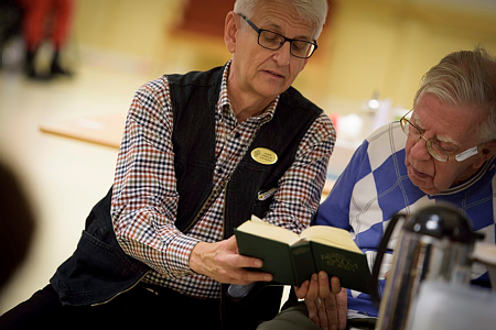 Två äldre män sjunger tillsammans ur samma psalmbok.