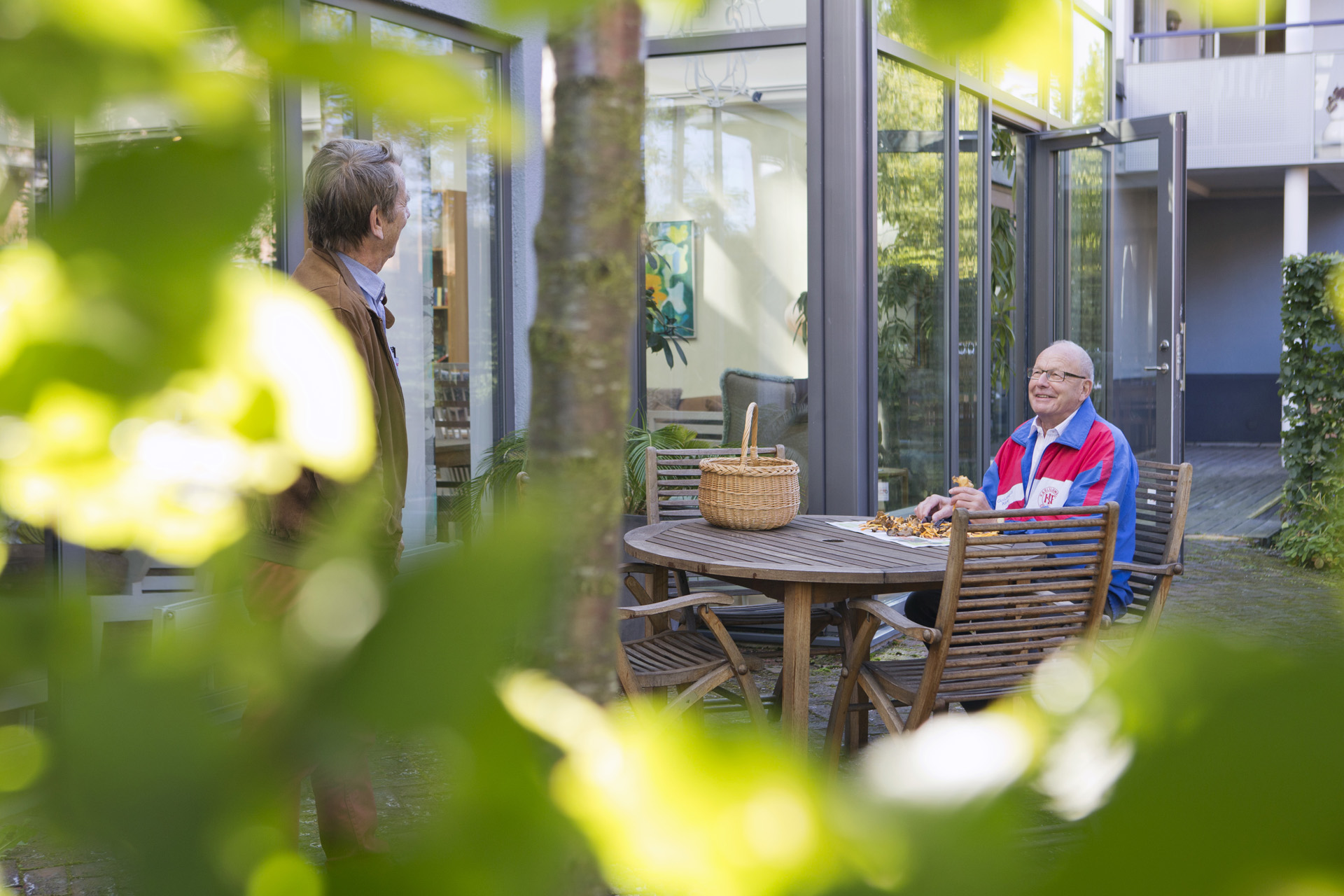 Bilden visar innegården på seniorbostäderna Laurentiusgården. En man sitter vid ett bord och rensar kantareller. 