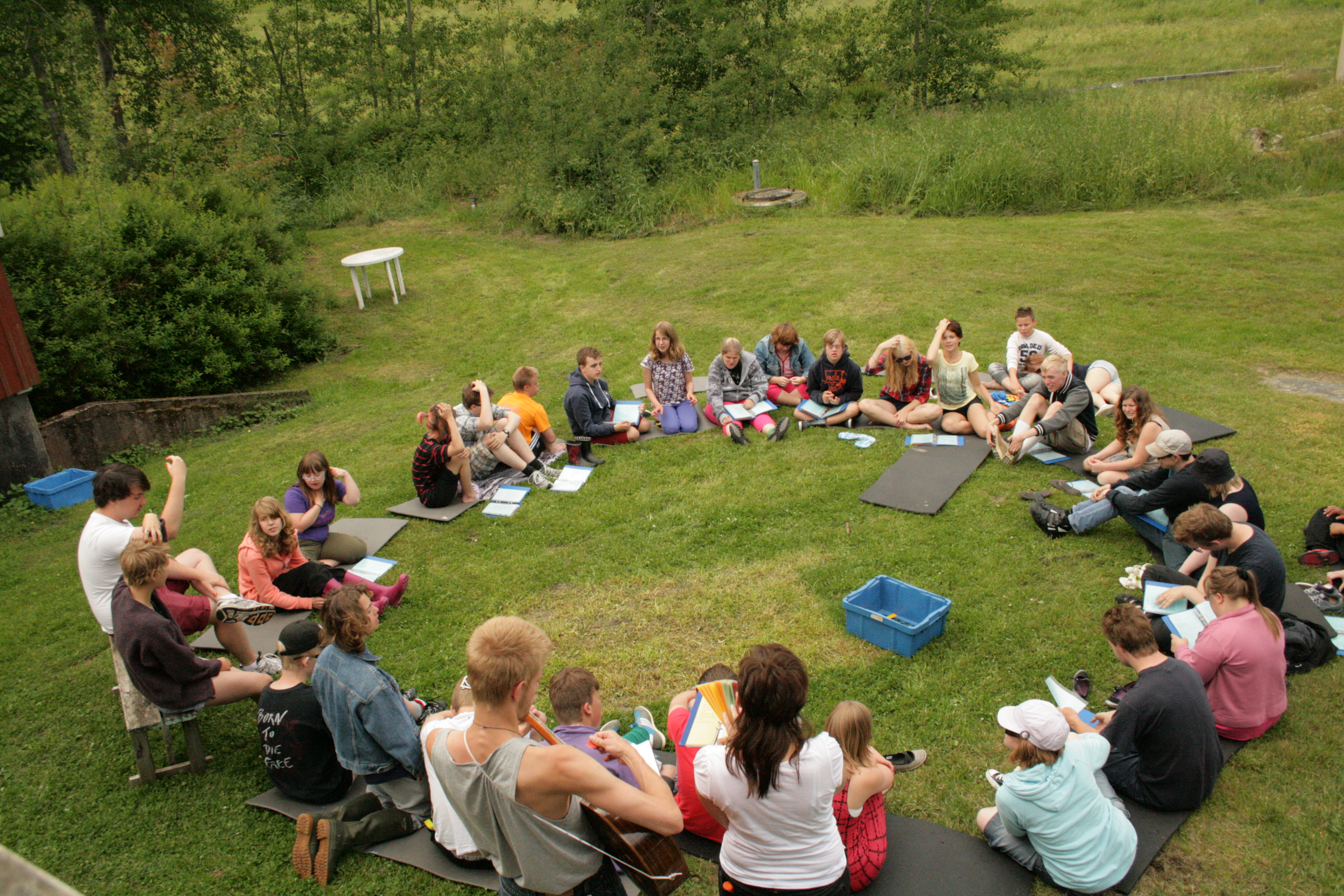 Ett antal personer sitter i en rund ring på en gräsmatta. 