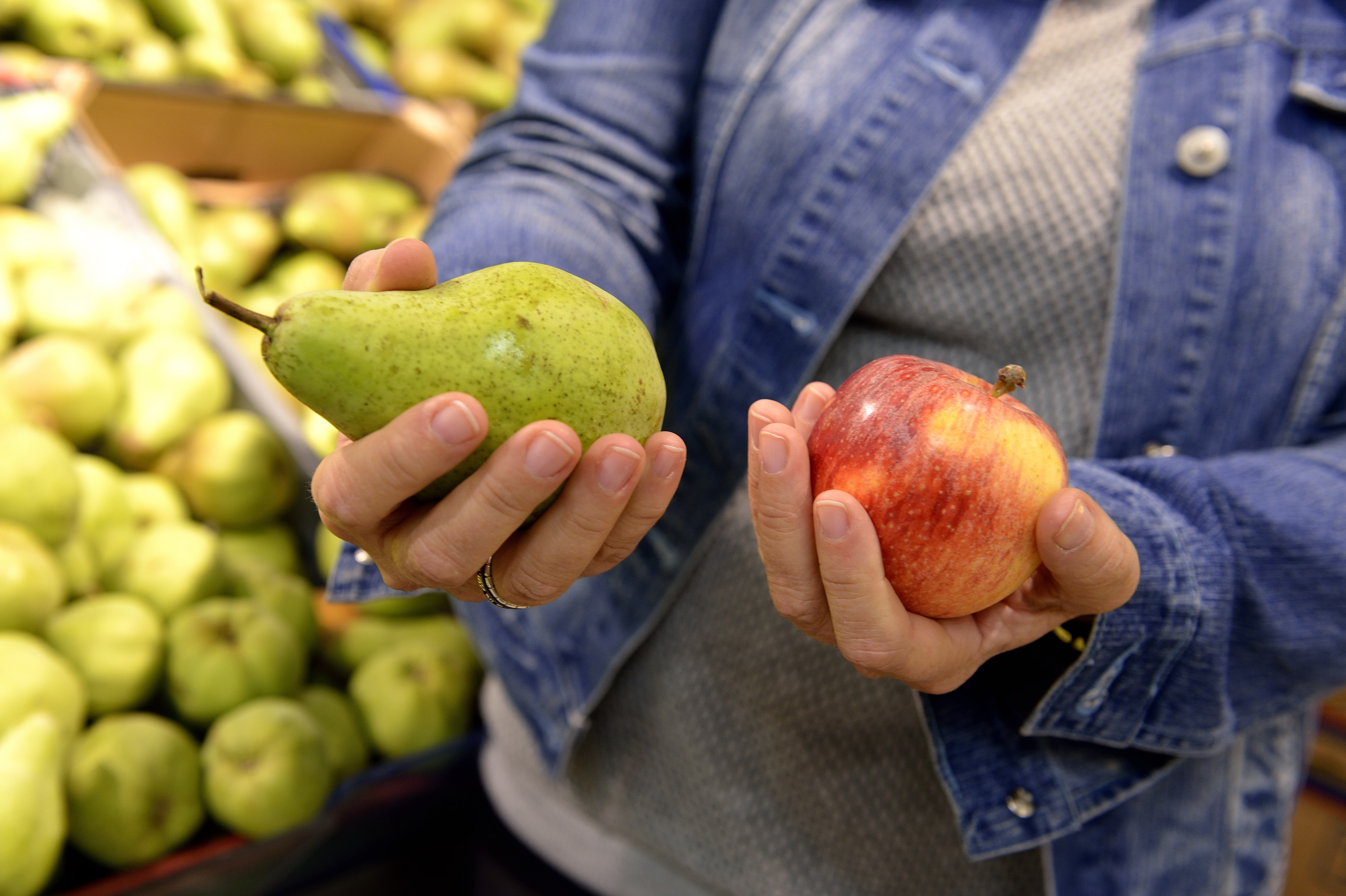 Någon står i mataffären och håller ett päron i ena handen och ett äpple i andra.