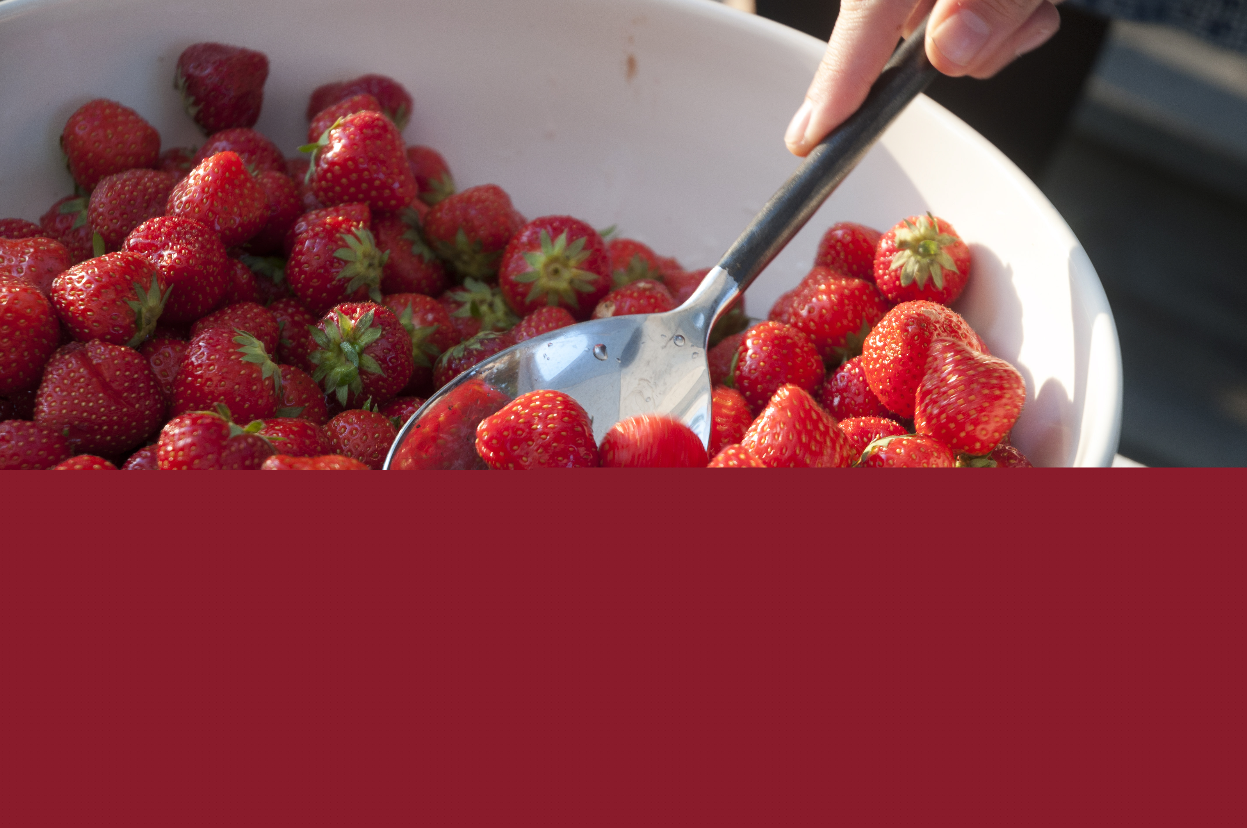 Någon tar jordgubbar ur en stor skål.