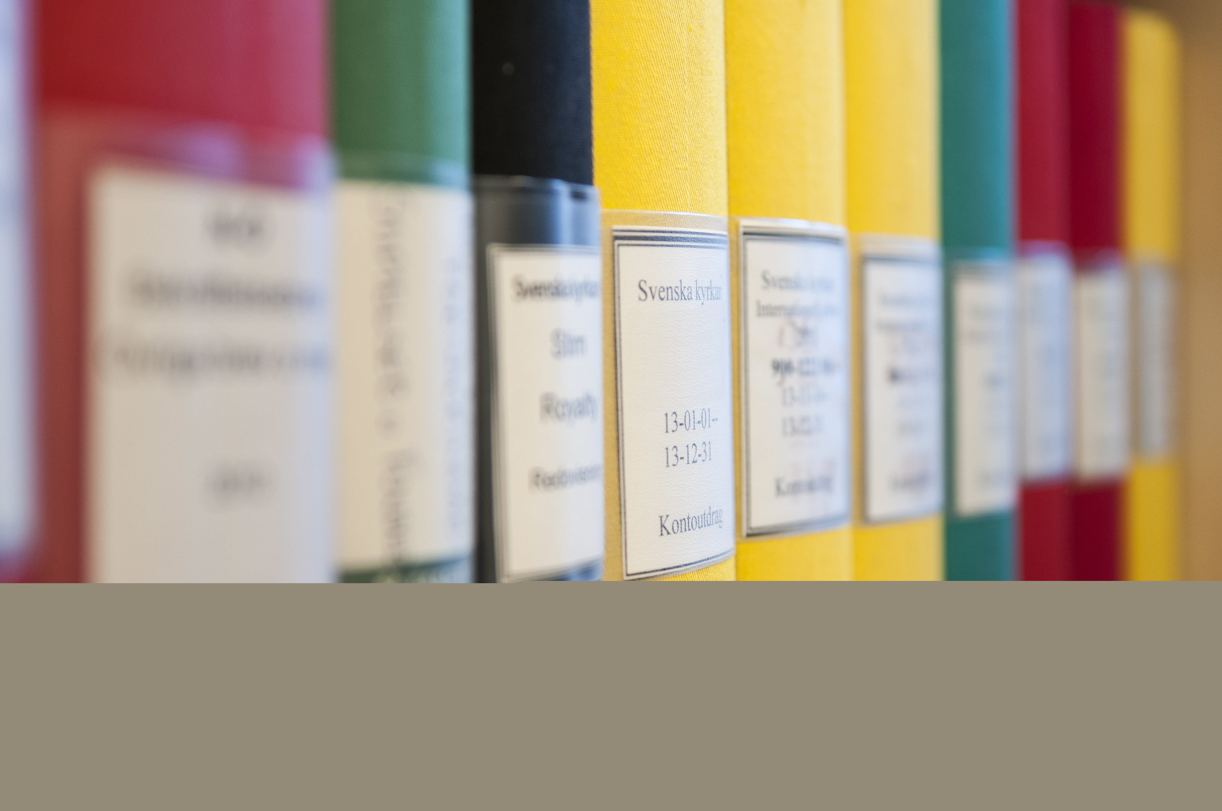 Pärmar i olika färger står på rad i hyllan.