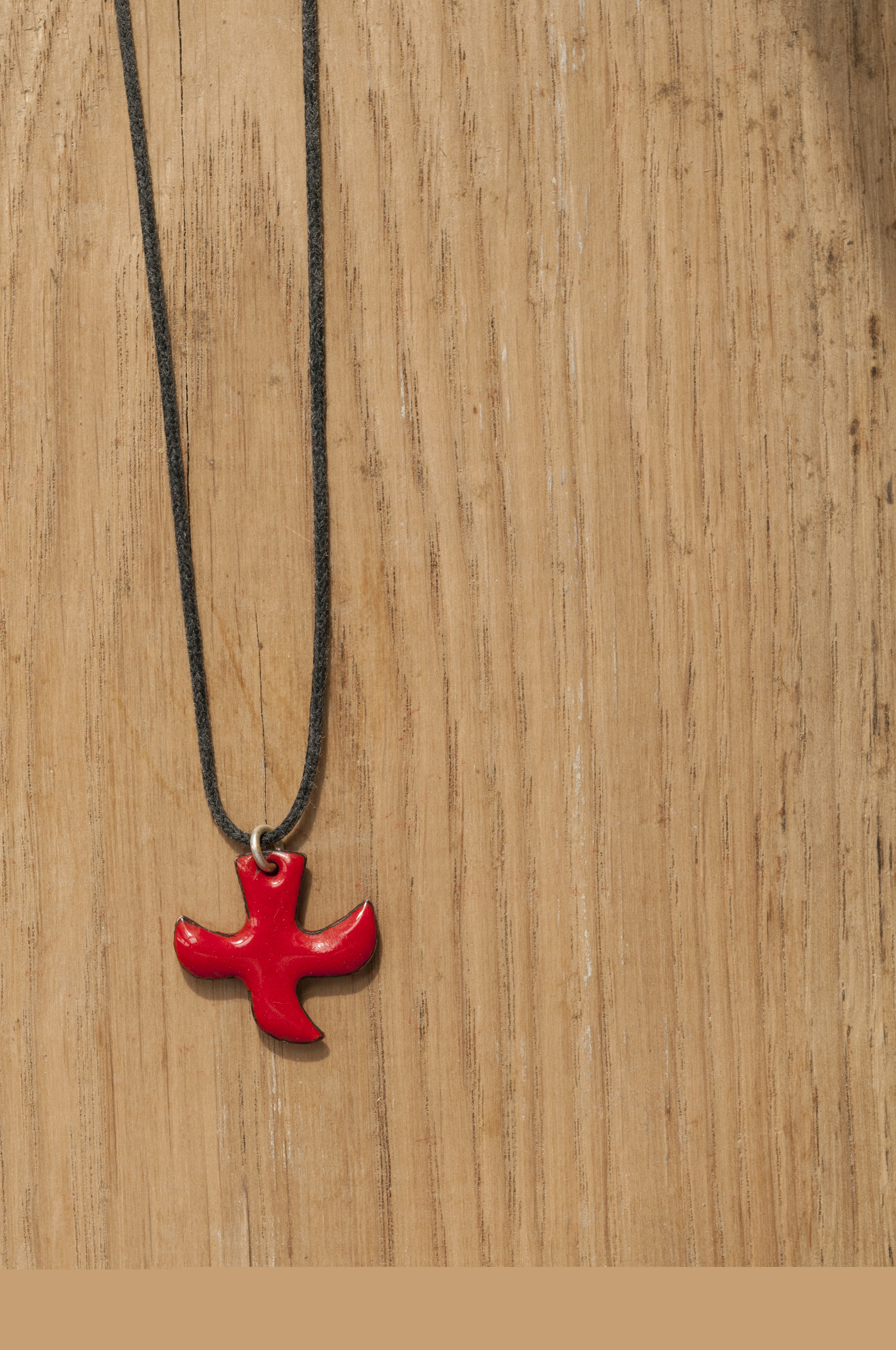 Ett halsband med ett rött Taizékors mot träbakgrund.