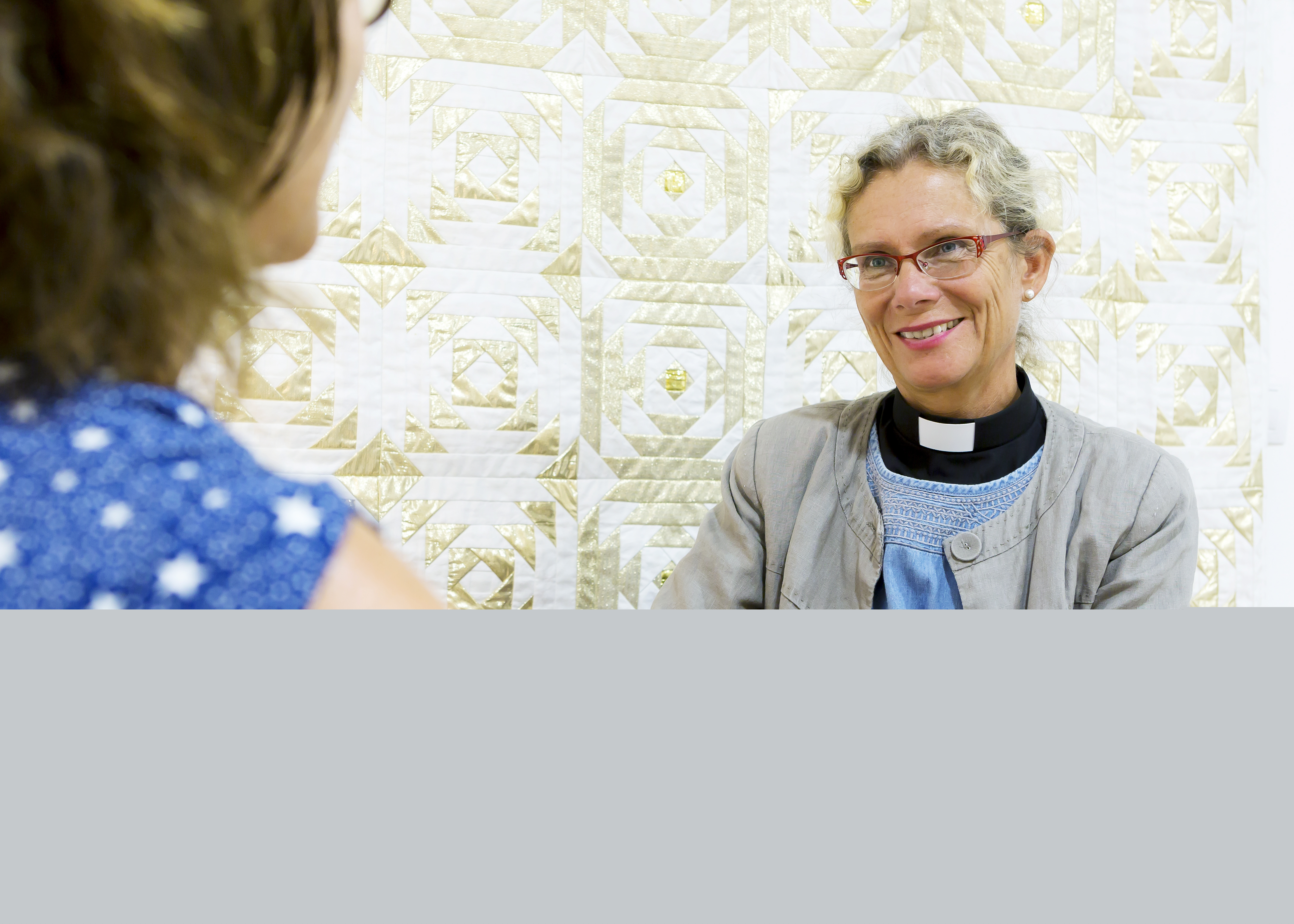 En kvinnlig präst samtalar med en kvinna inomhus.