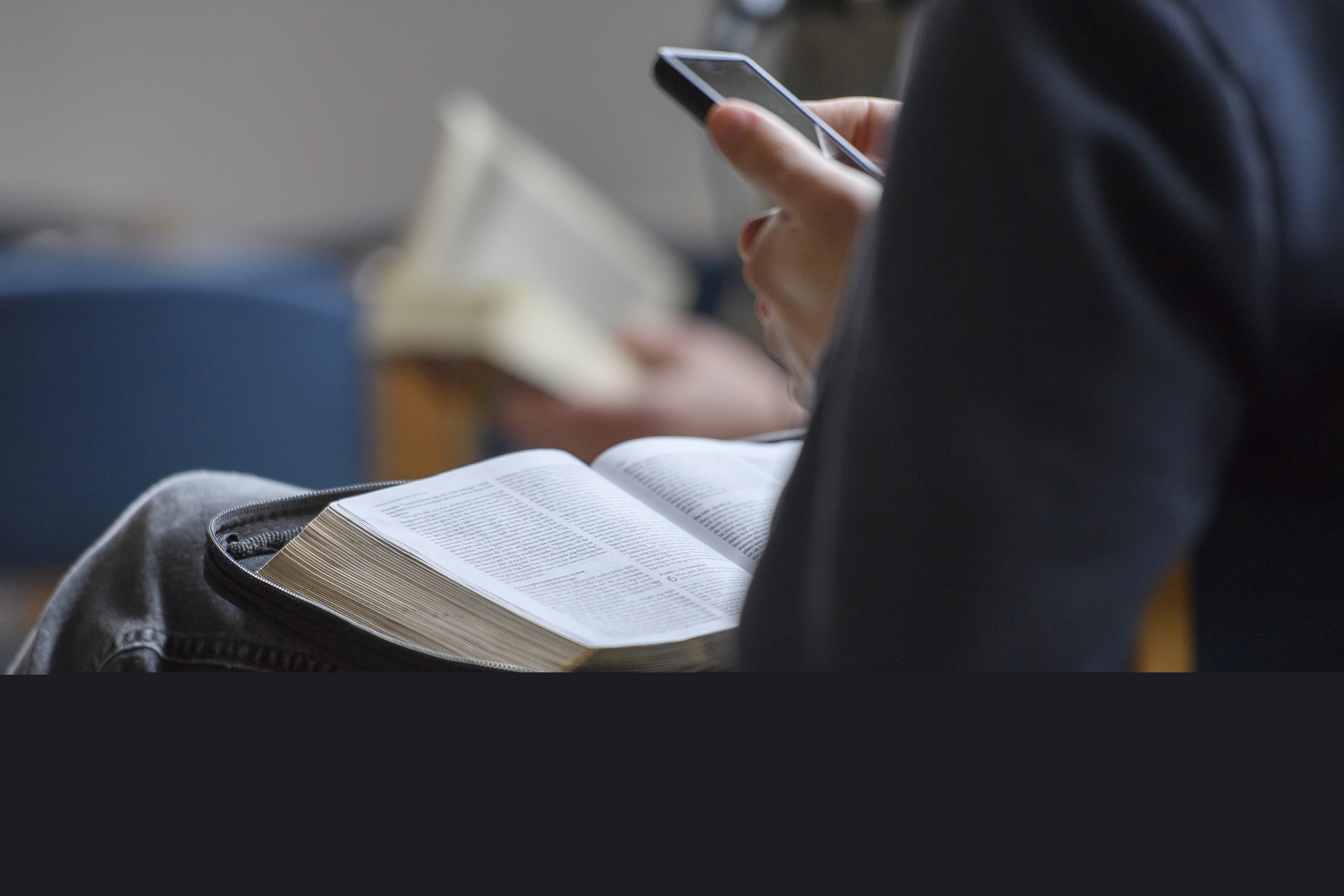 Någon sitter med en bok i knät och mobiltelefonen i handen.