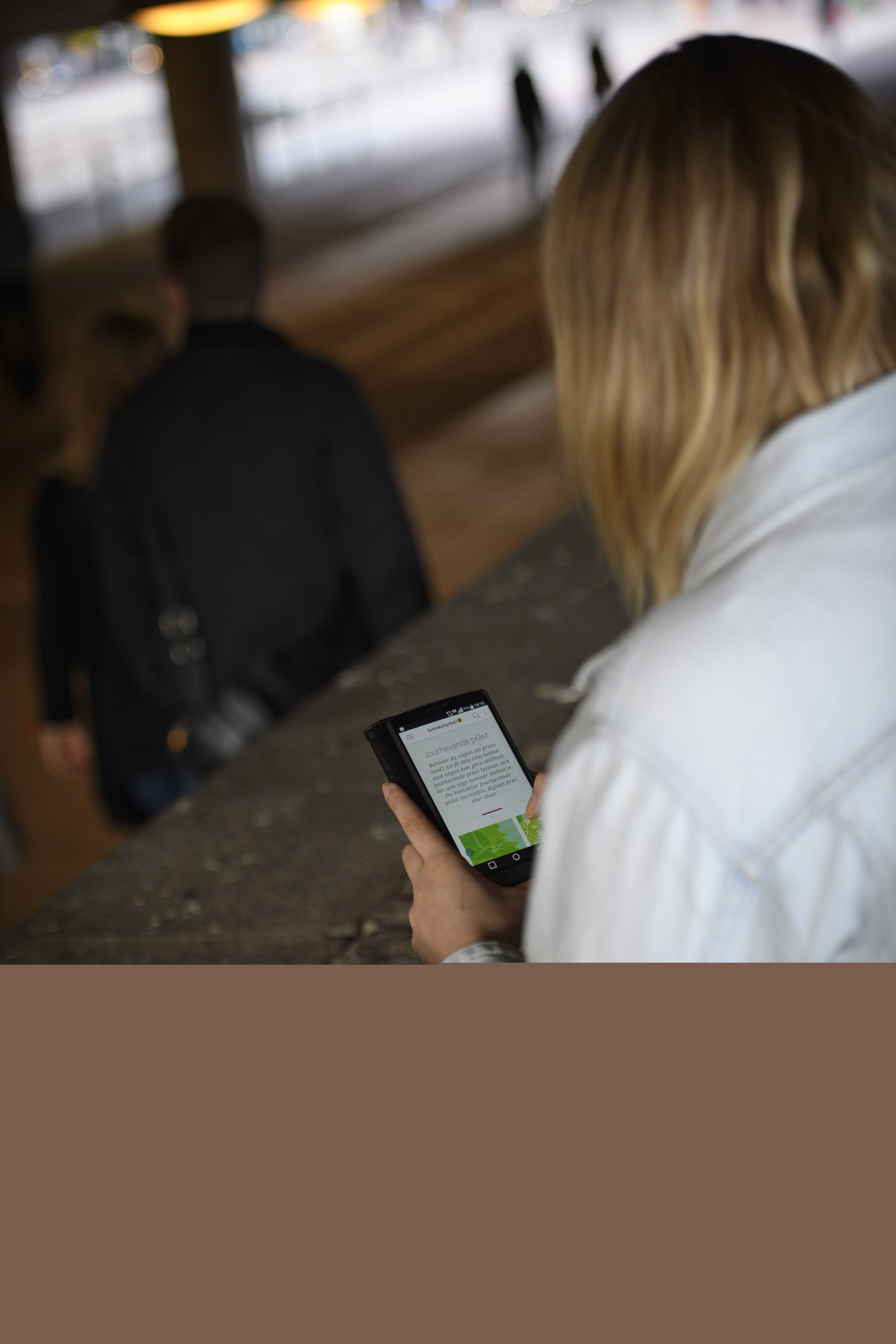 En kvinna sitter utomhus och håller på med sin mobiltelefon.