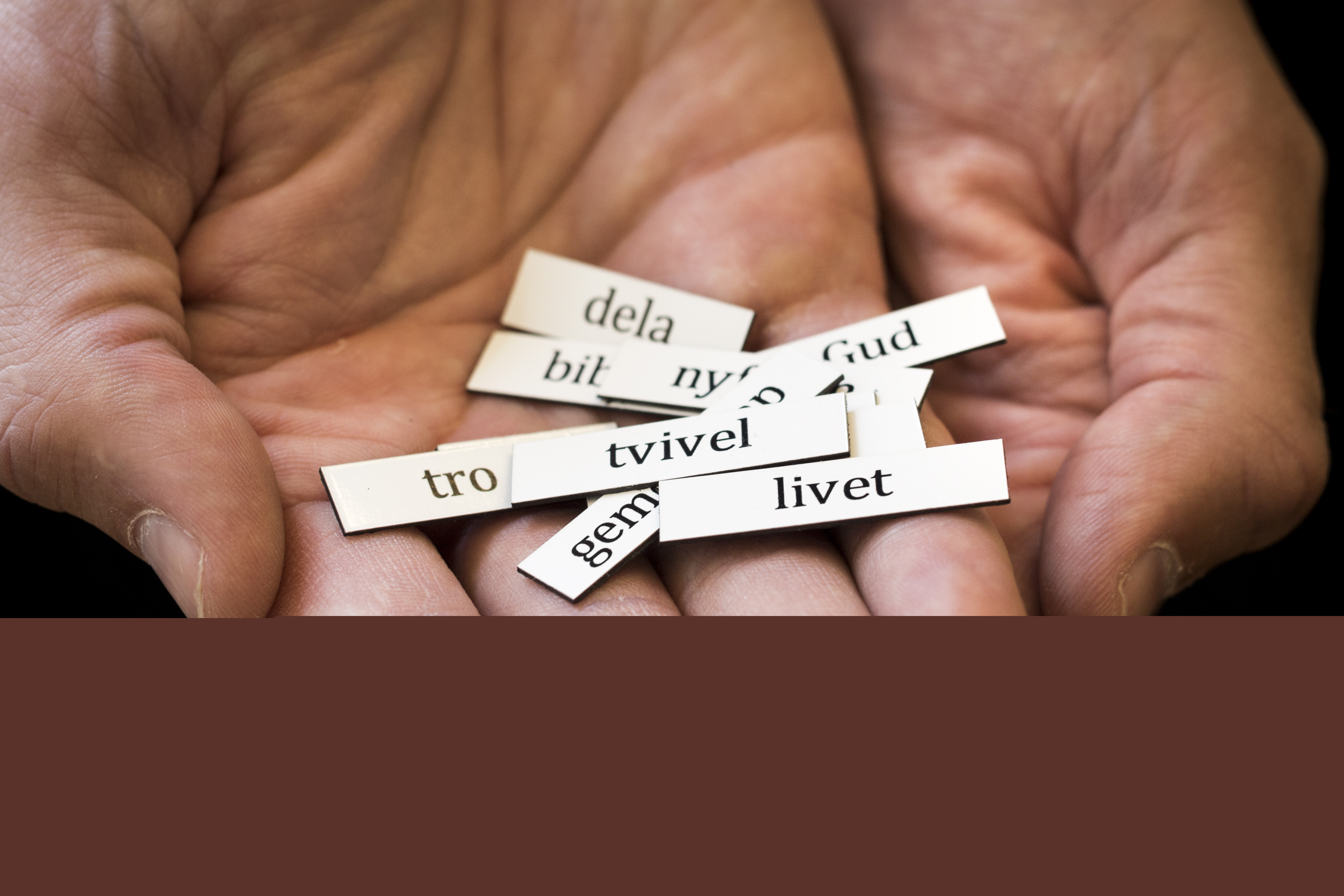 Närbild på någon som håller fram några kylskåpsmagneter med ord som tvivel, livet, Gud, dela, tro och så vidare.