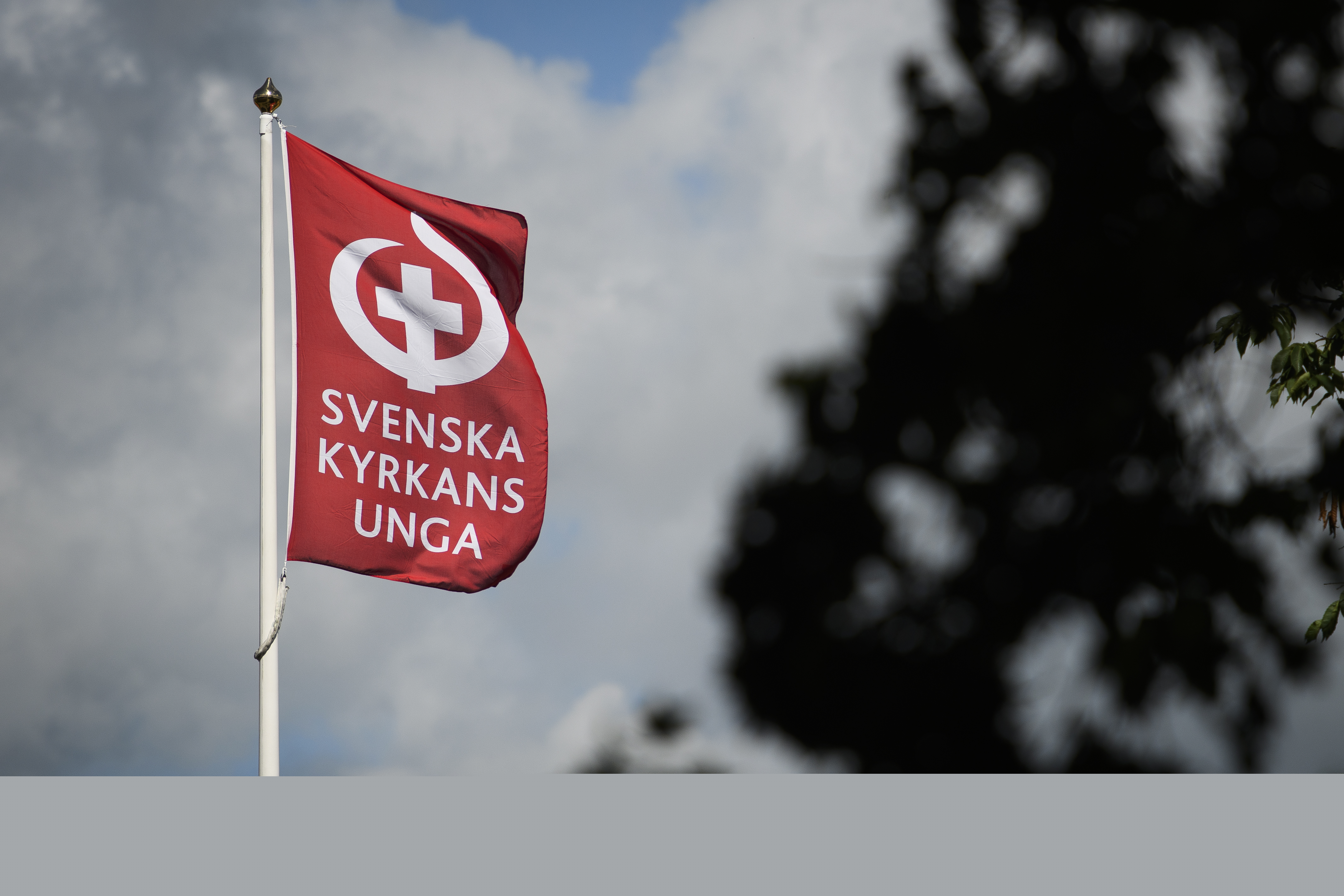 En flaggstång med en röd flagga med texten Svenska kyrkans unga och deras symbol.