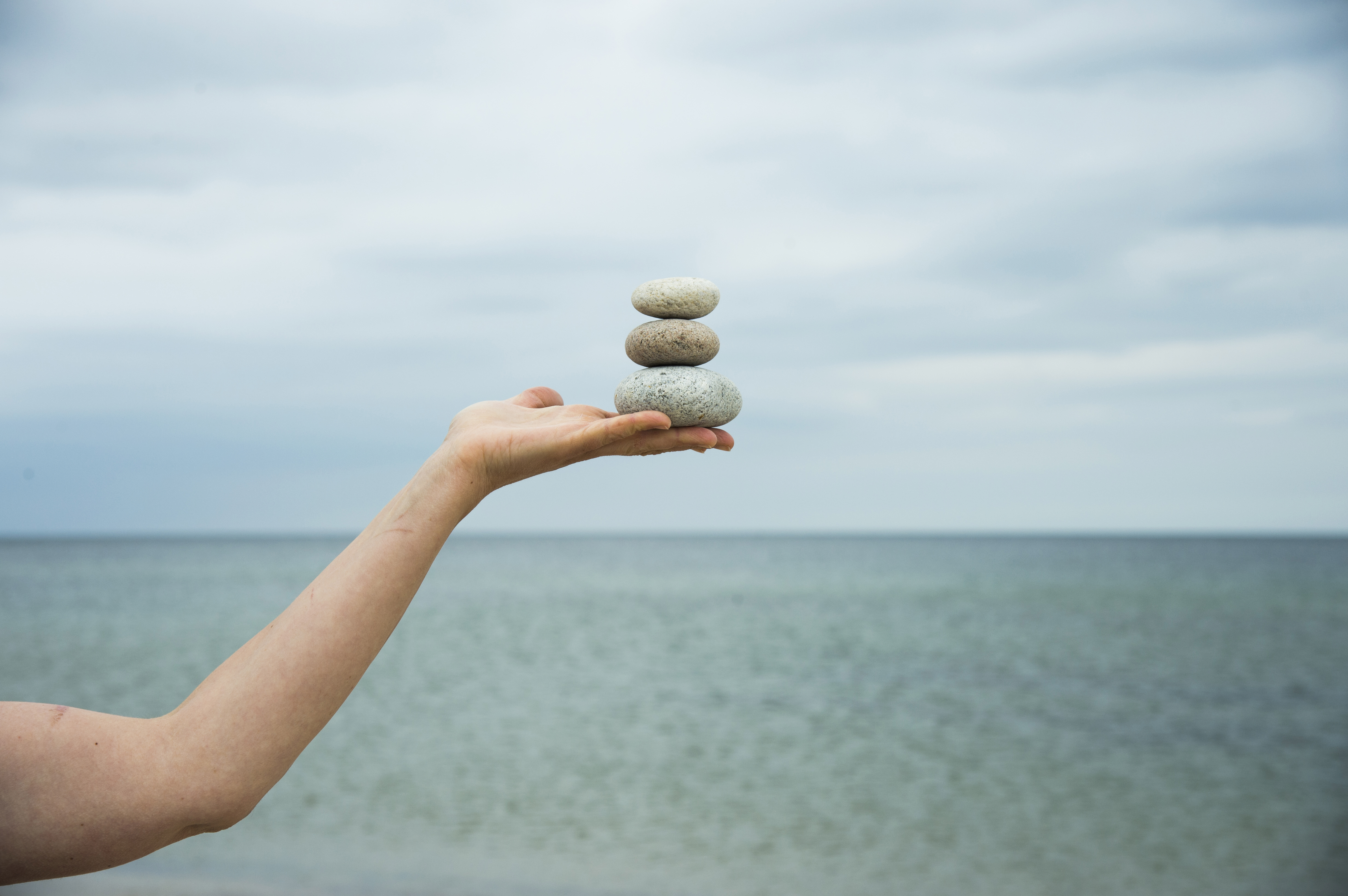 Någon står vid vattnet och balanser tre stenar på varandra i handen.