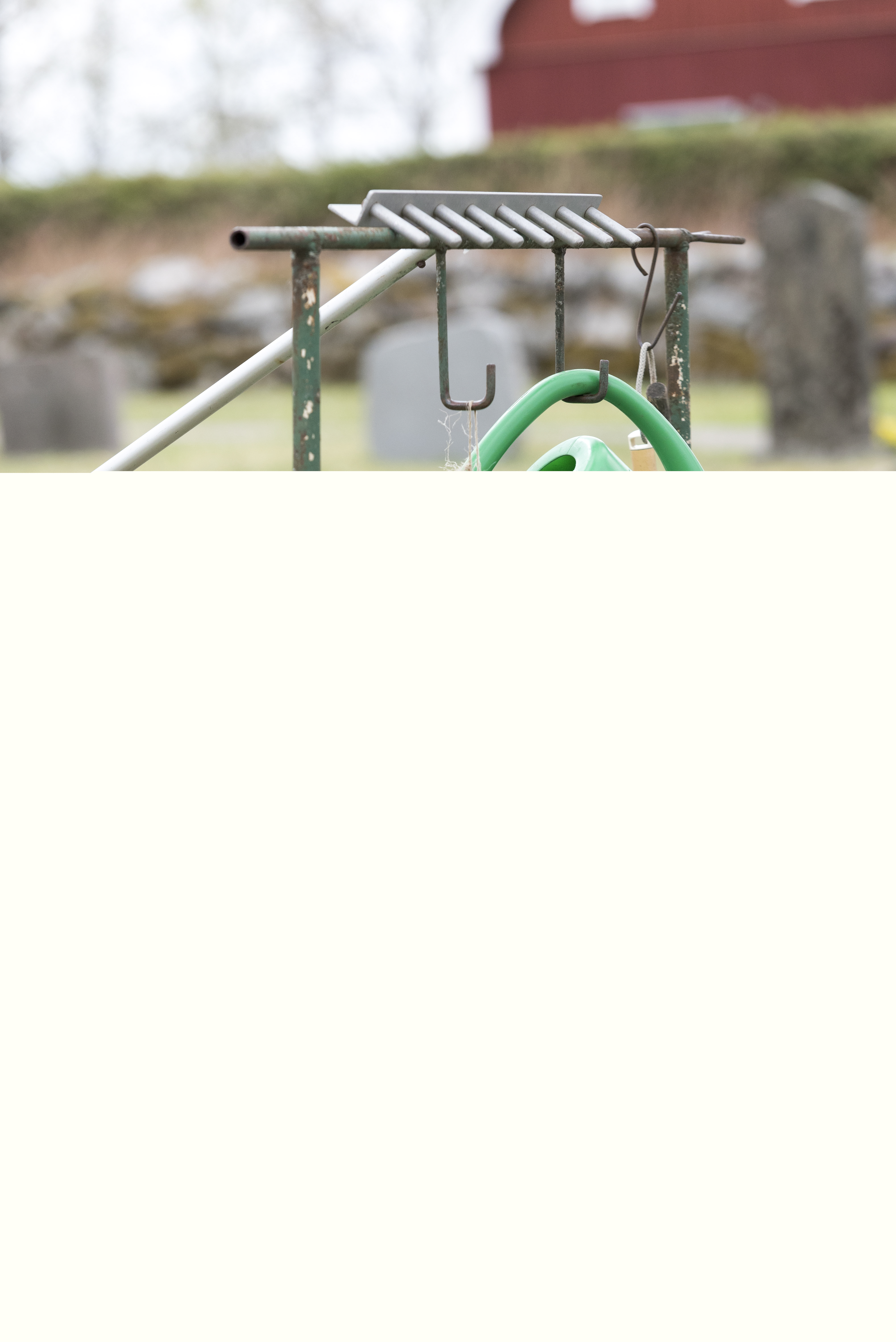 En vattenkanna och några verktyg hänger på en ställning vid en kyrkogård.