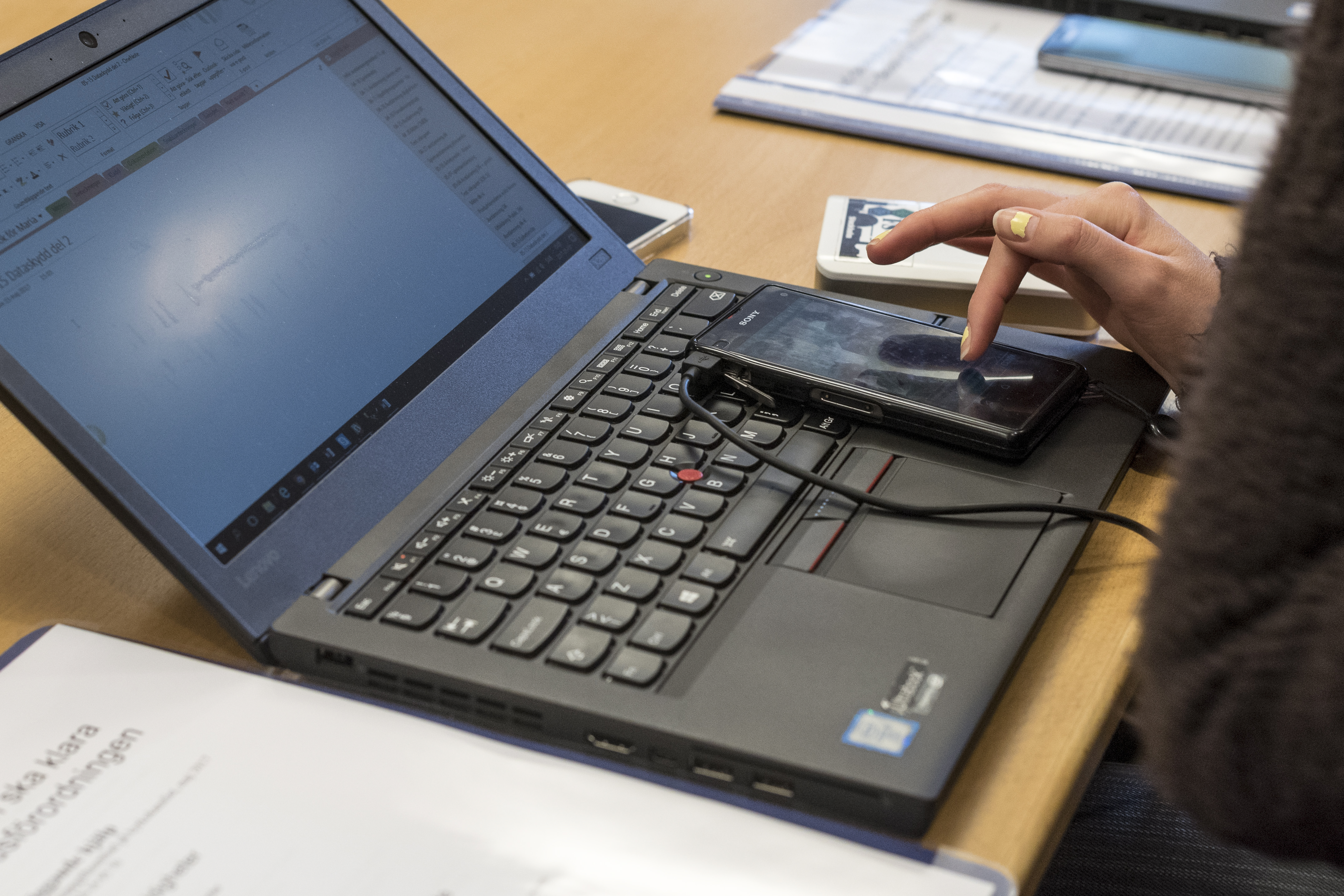 På en uppslagen laptop ligger en mobiltelefon som någon har sitt pekfinger på.
