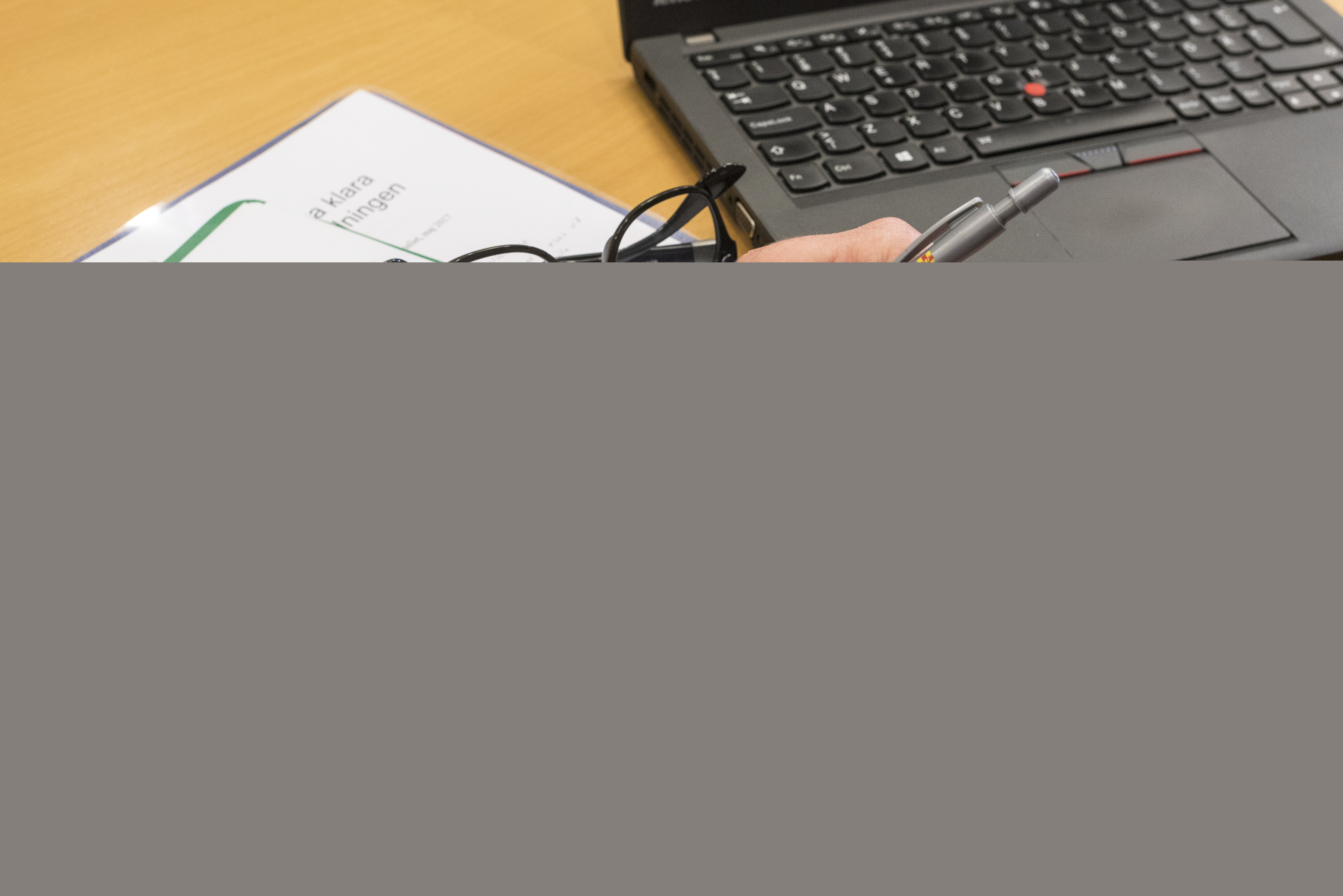 En person med en penna i handen sitter med ett texthäfte och en dator framför sig.