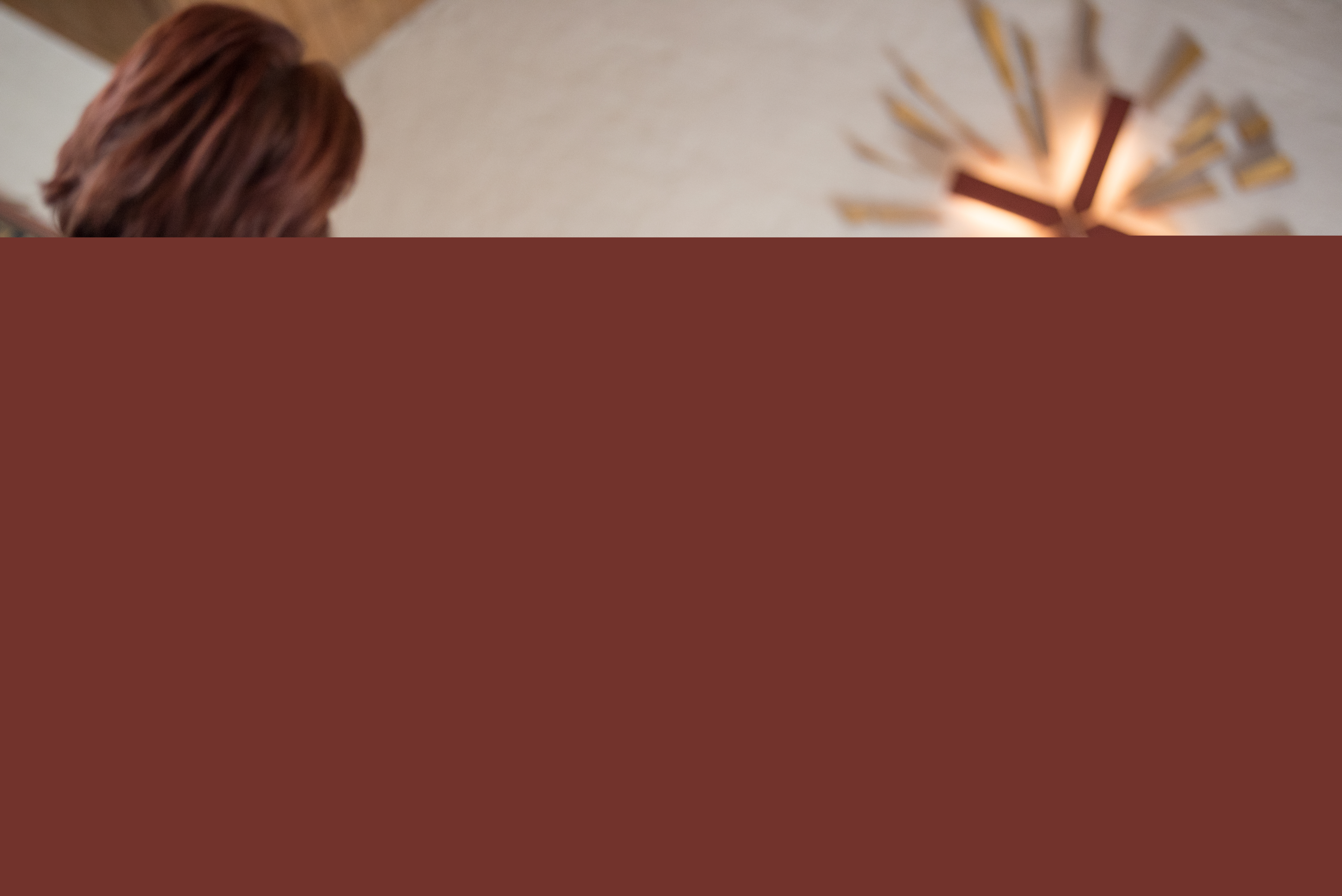 En liten flicka sitter i kyrkbänken och håller ett palmblad över huvudet. En präst i blå kåpa syns suddigt i bakgrunden.