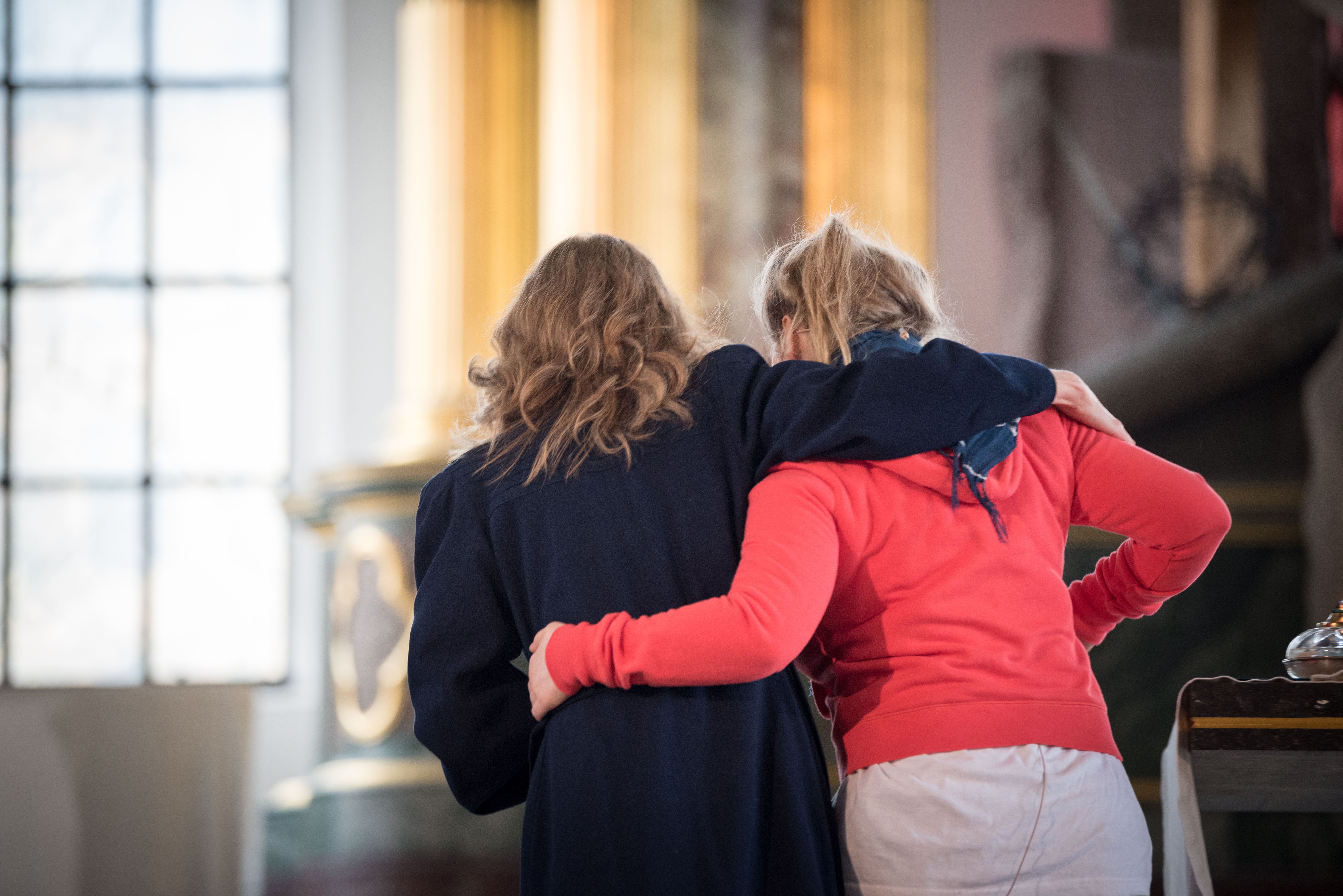 Två kvinnor med armarna om varandra hjälps åt att sätta sig tillrätta i kyrkbänken.