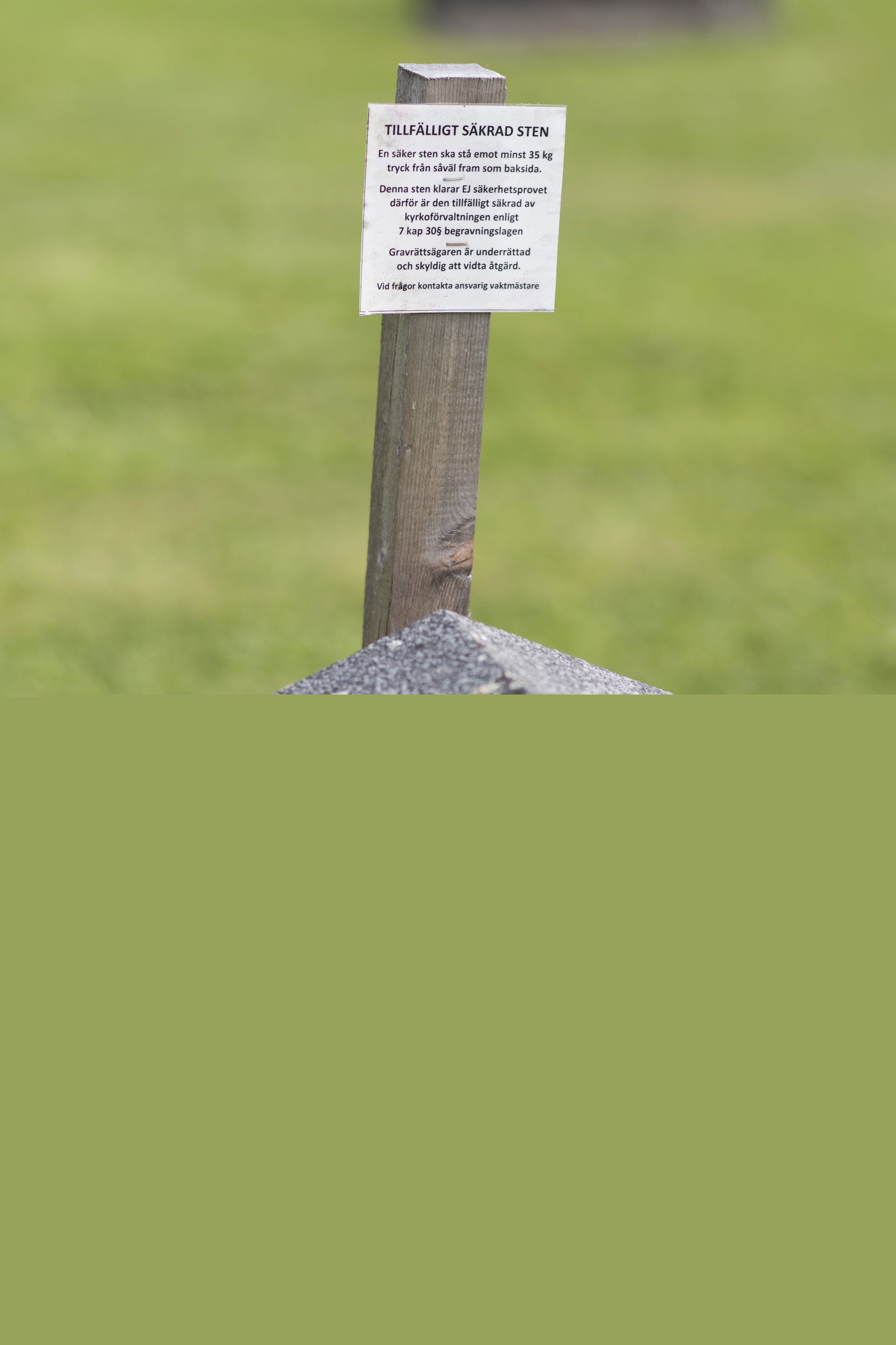 En ostadig gravsten står lutad mot en trästolpe.