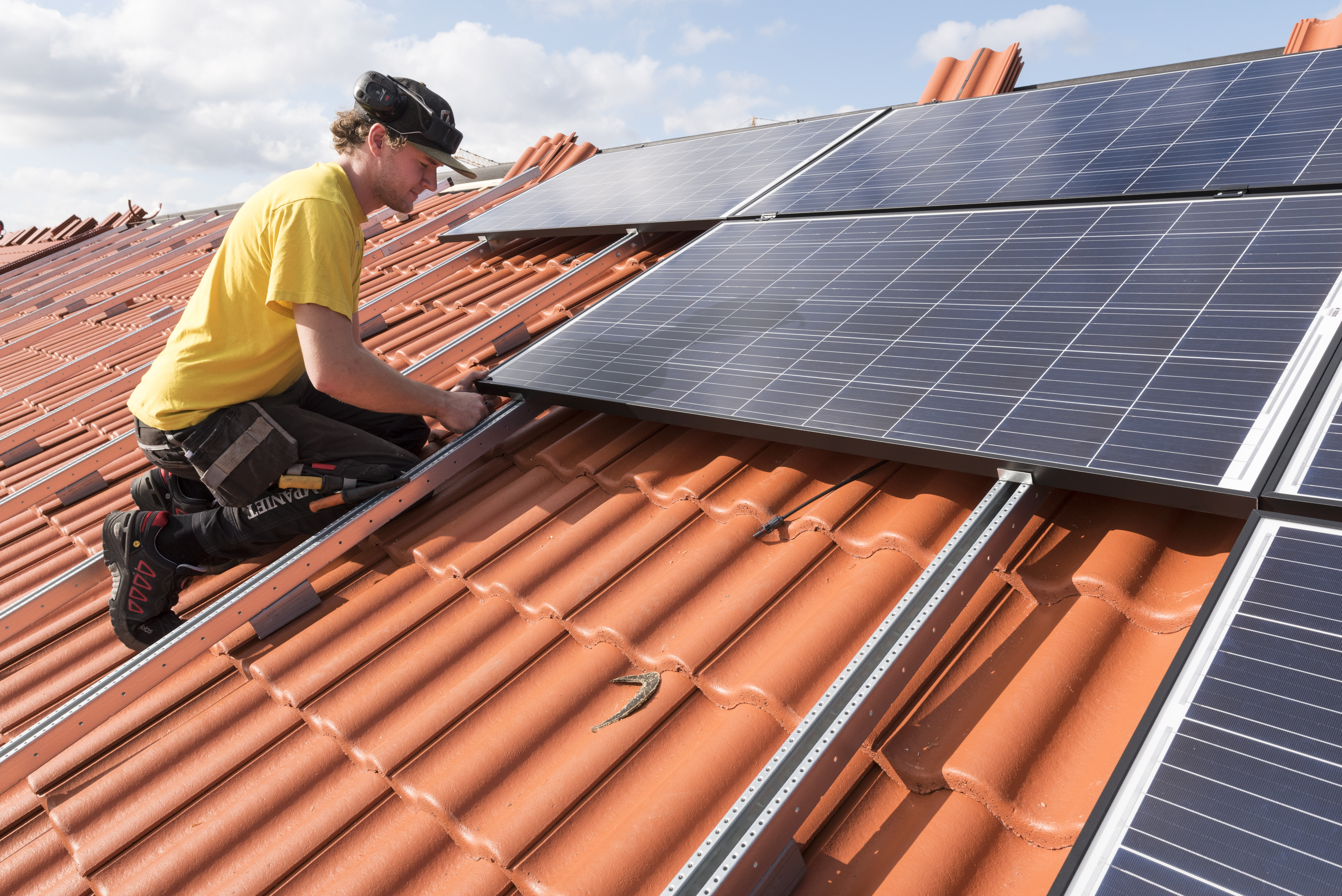 En byggarbetare monterar solceller på ett hustak.