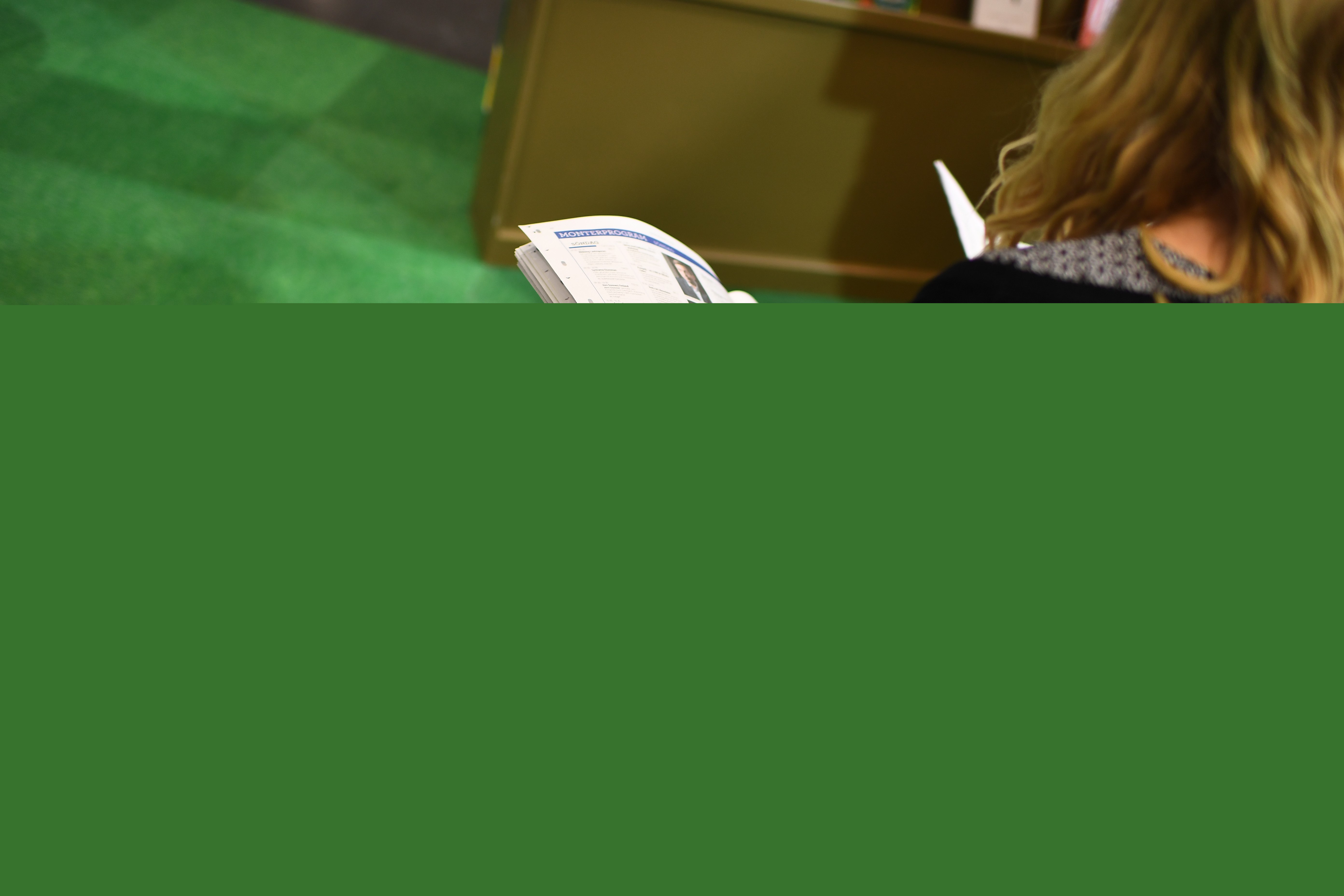 En kvinna sitter i en monter och bläddrar i en tidning.