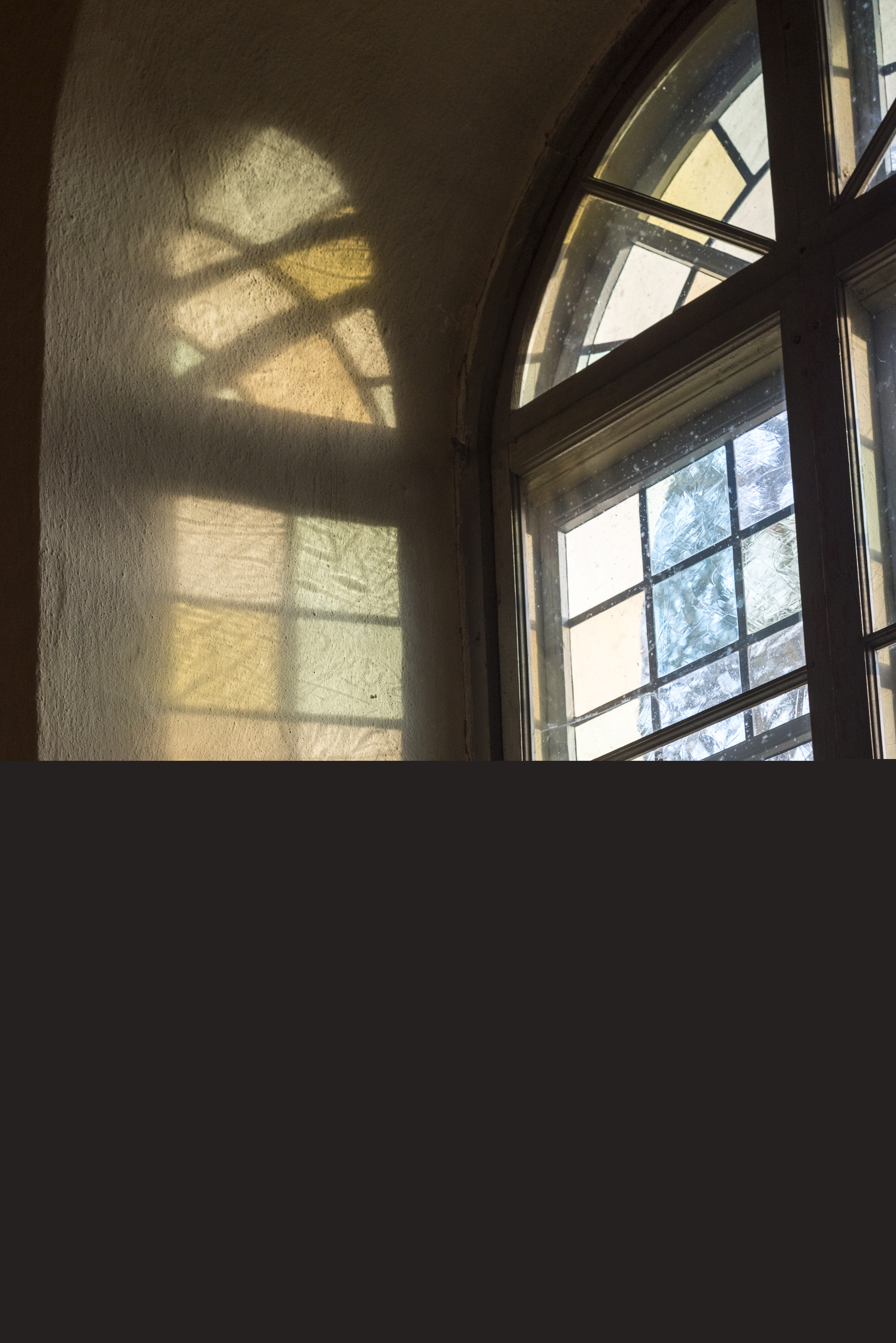 Solen reflekteras på en vit vägg genom ett färgat kyrkfönster.