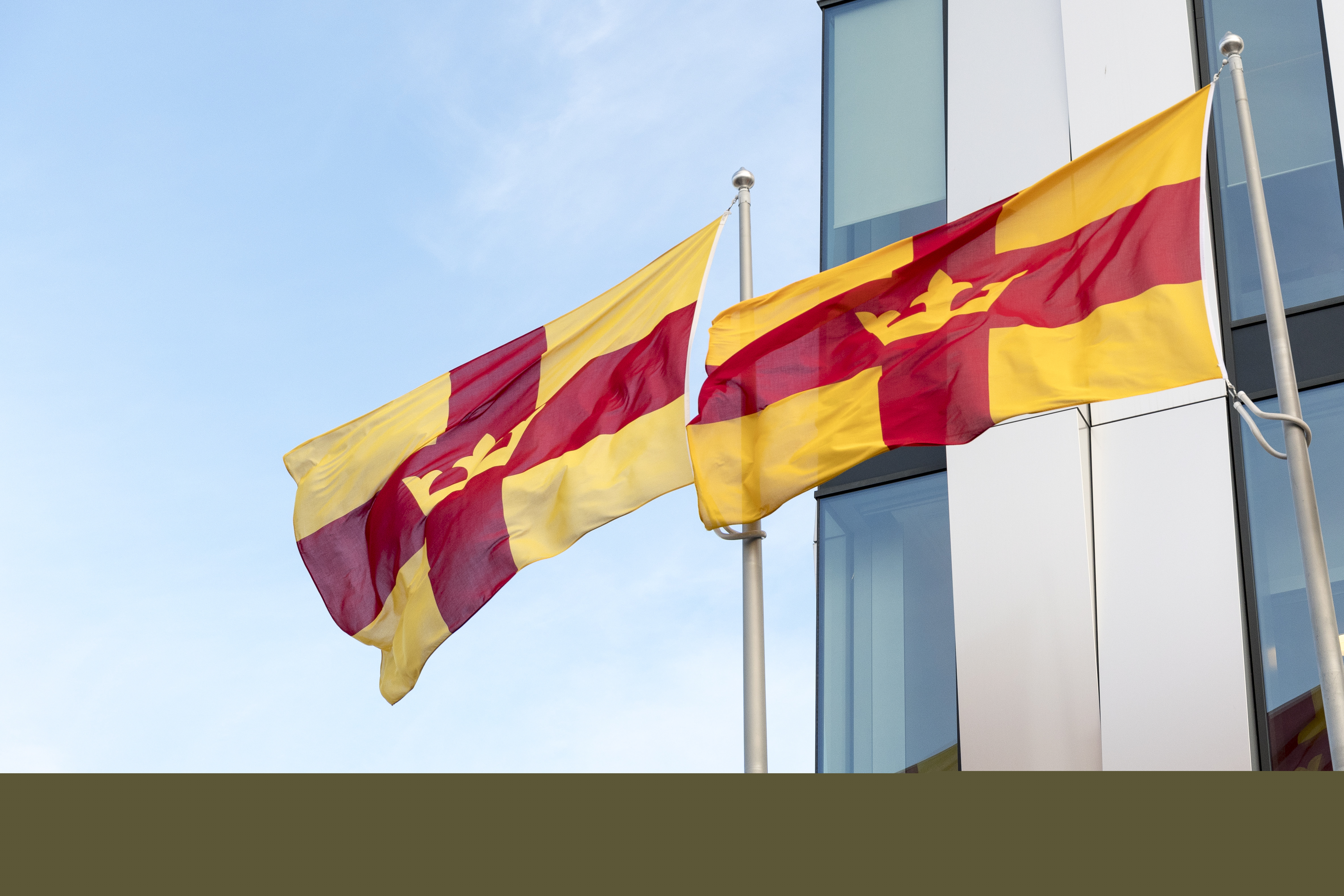 Två flaggstänger med Svenska kyrkans flagga utanför en byggnad.