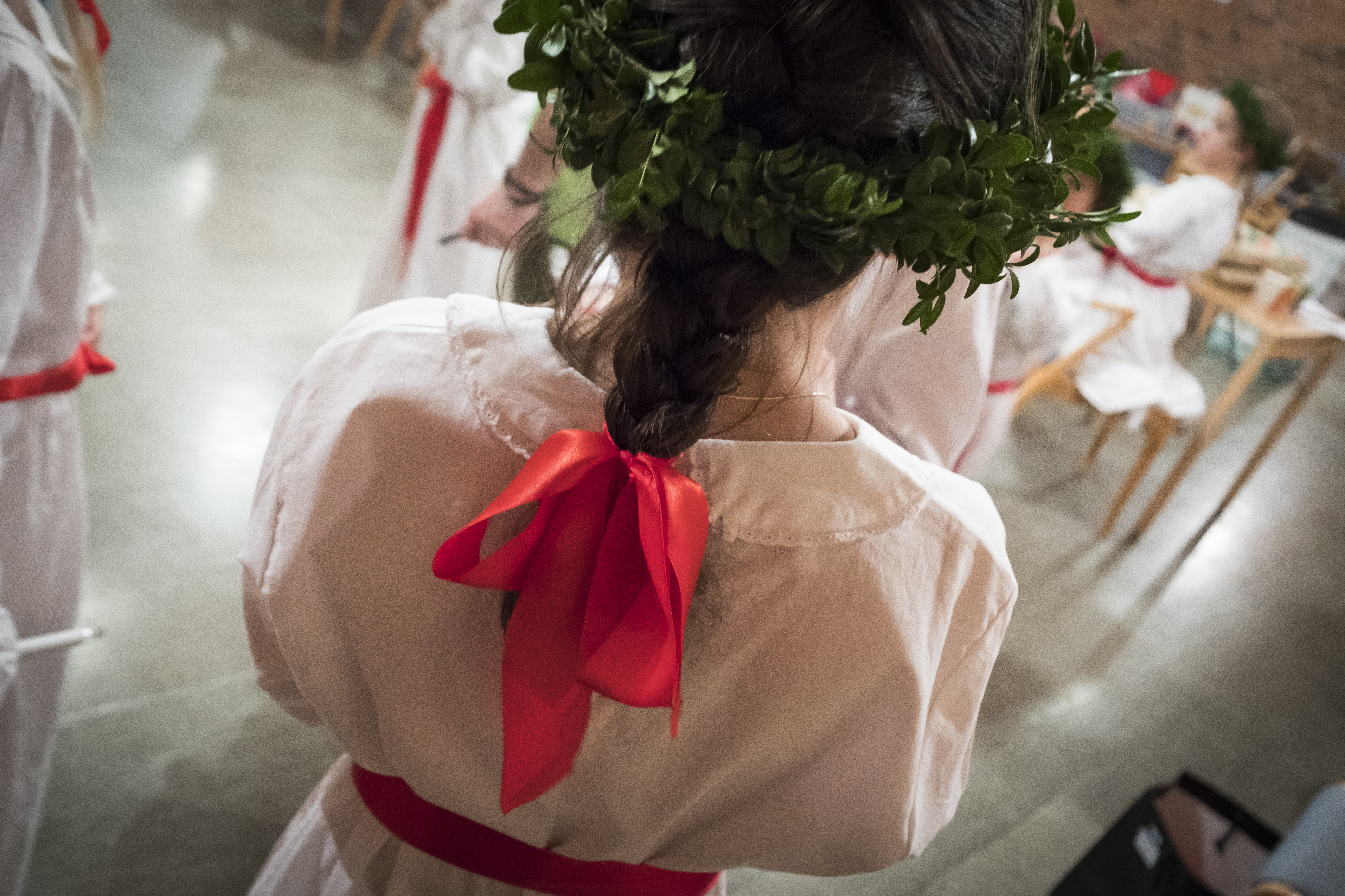 En flicka i luciakläder och krans, med ett rött sidenband som tofs i flätan.