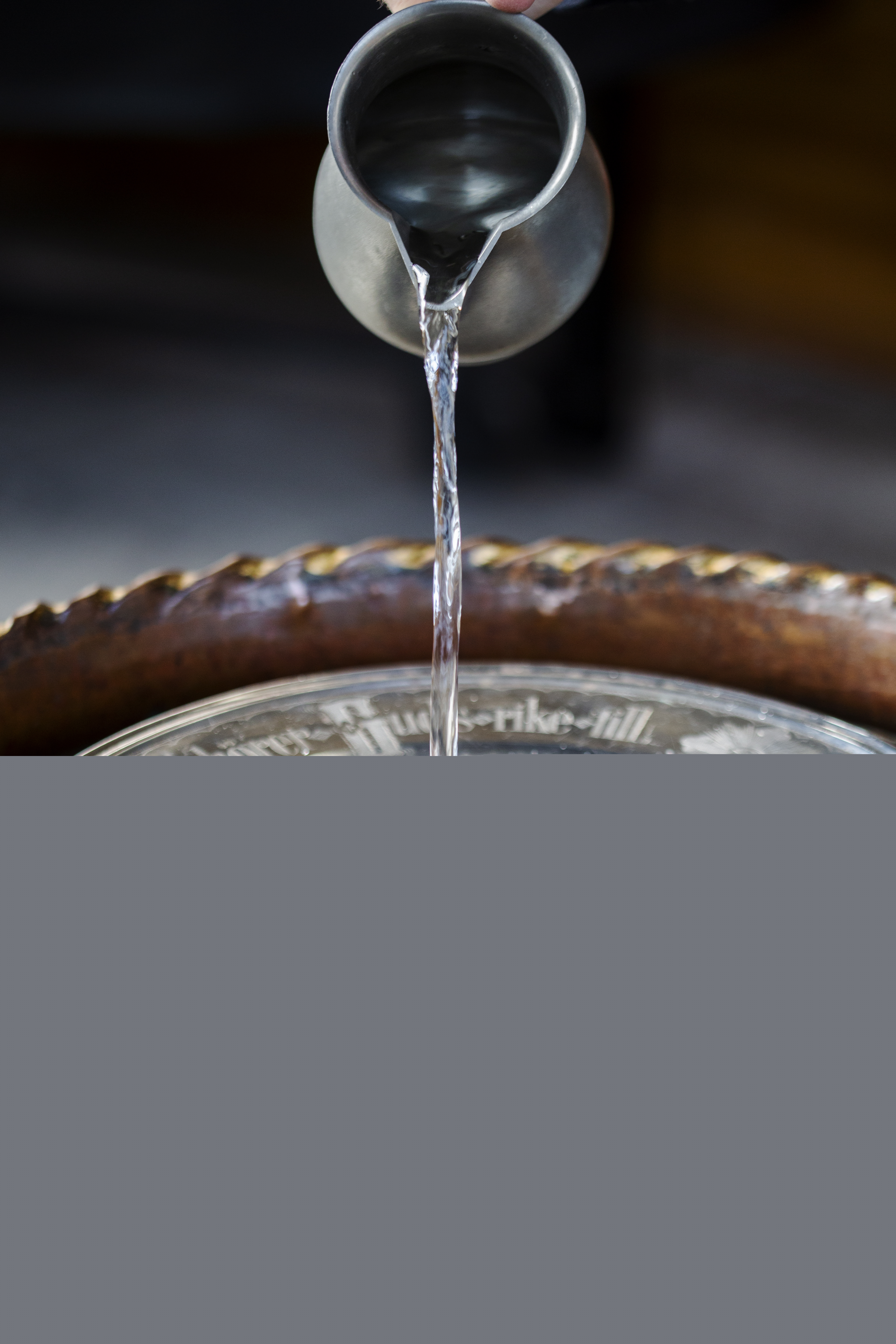 Någon häller vatten i dopfunten från en kanna.