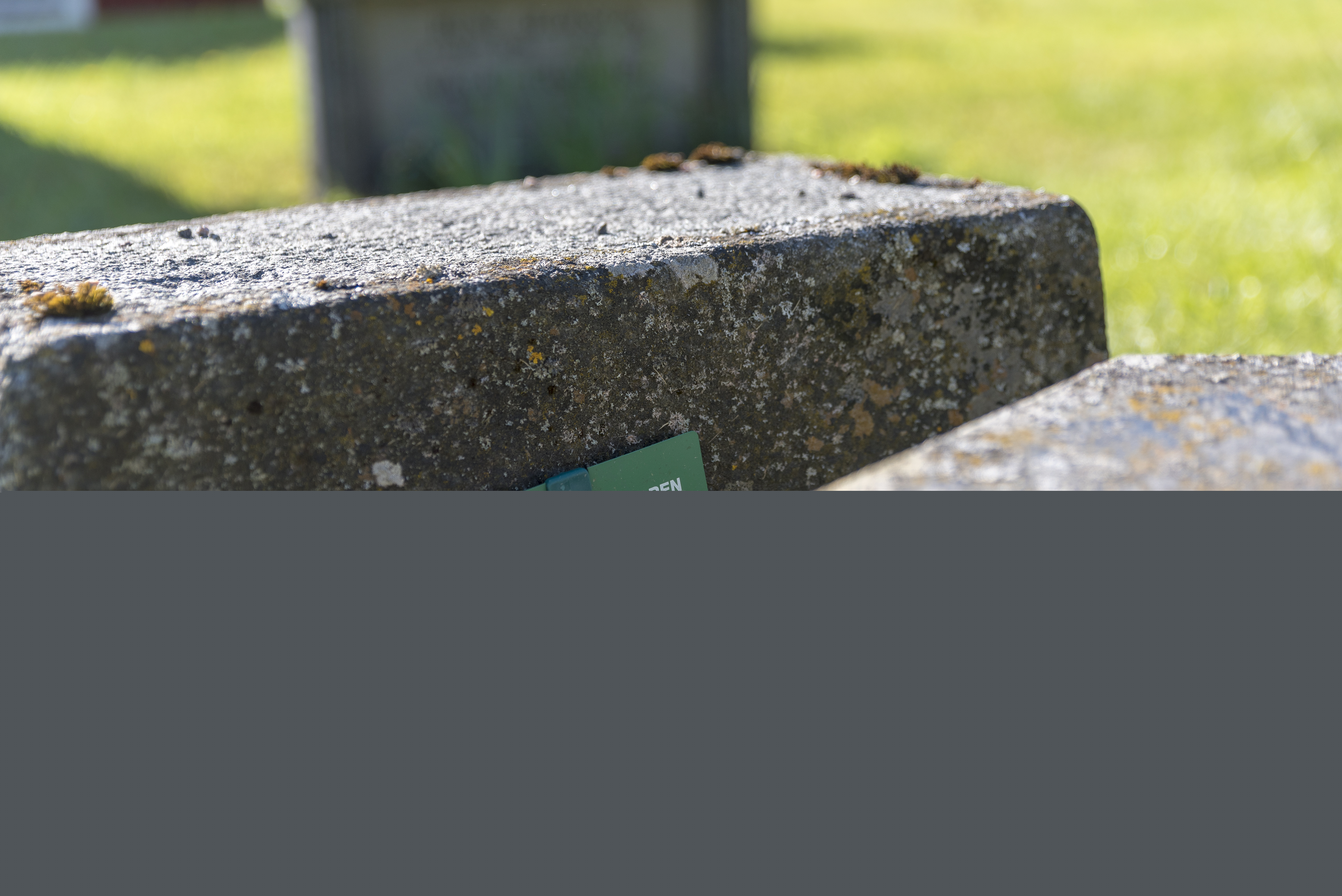 En liten skylt som gått sönder står vid en gravsten.