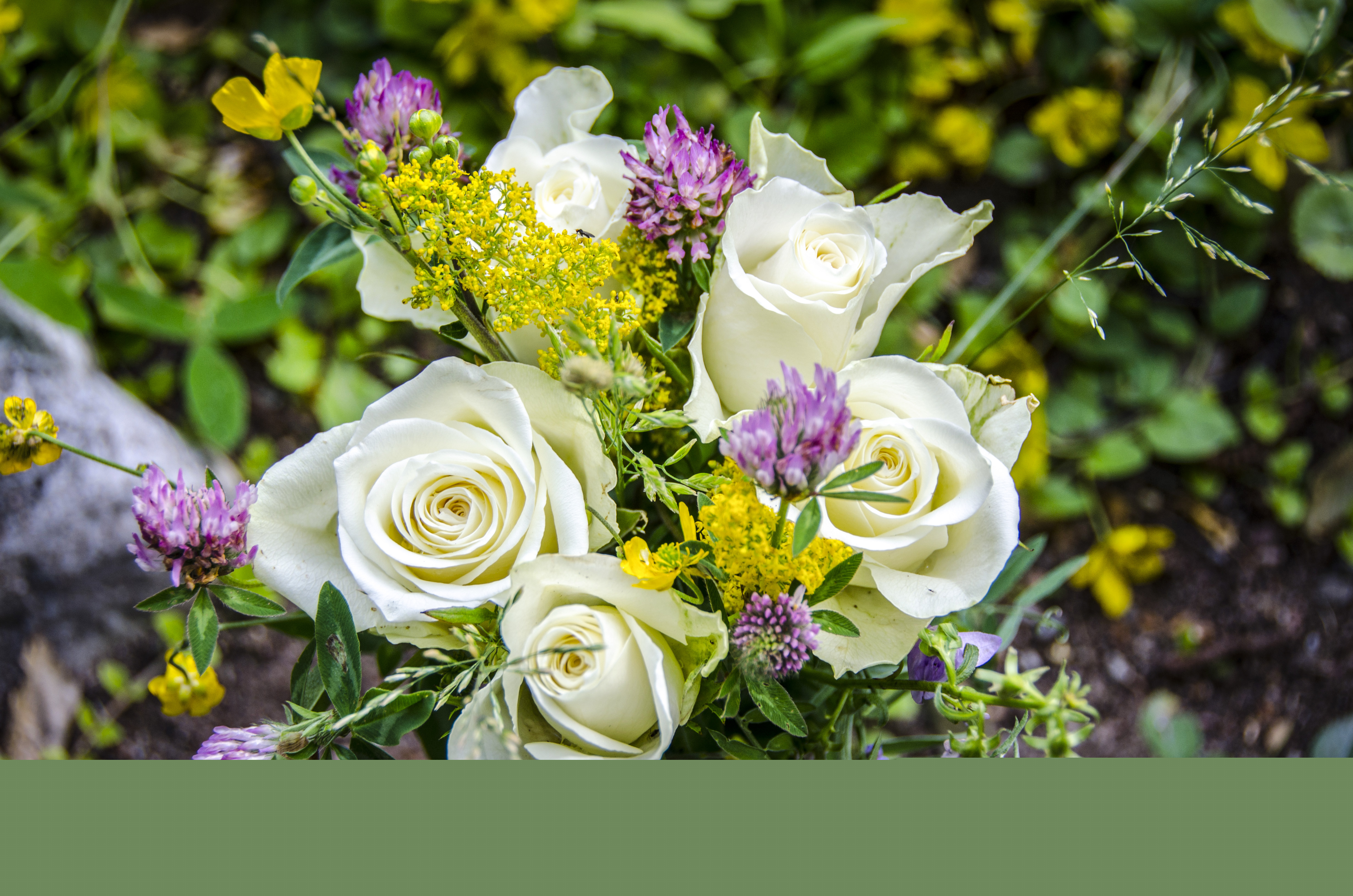 En bukett med vita rosor och vilda blommor.