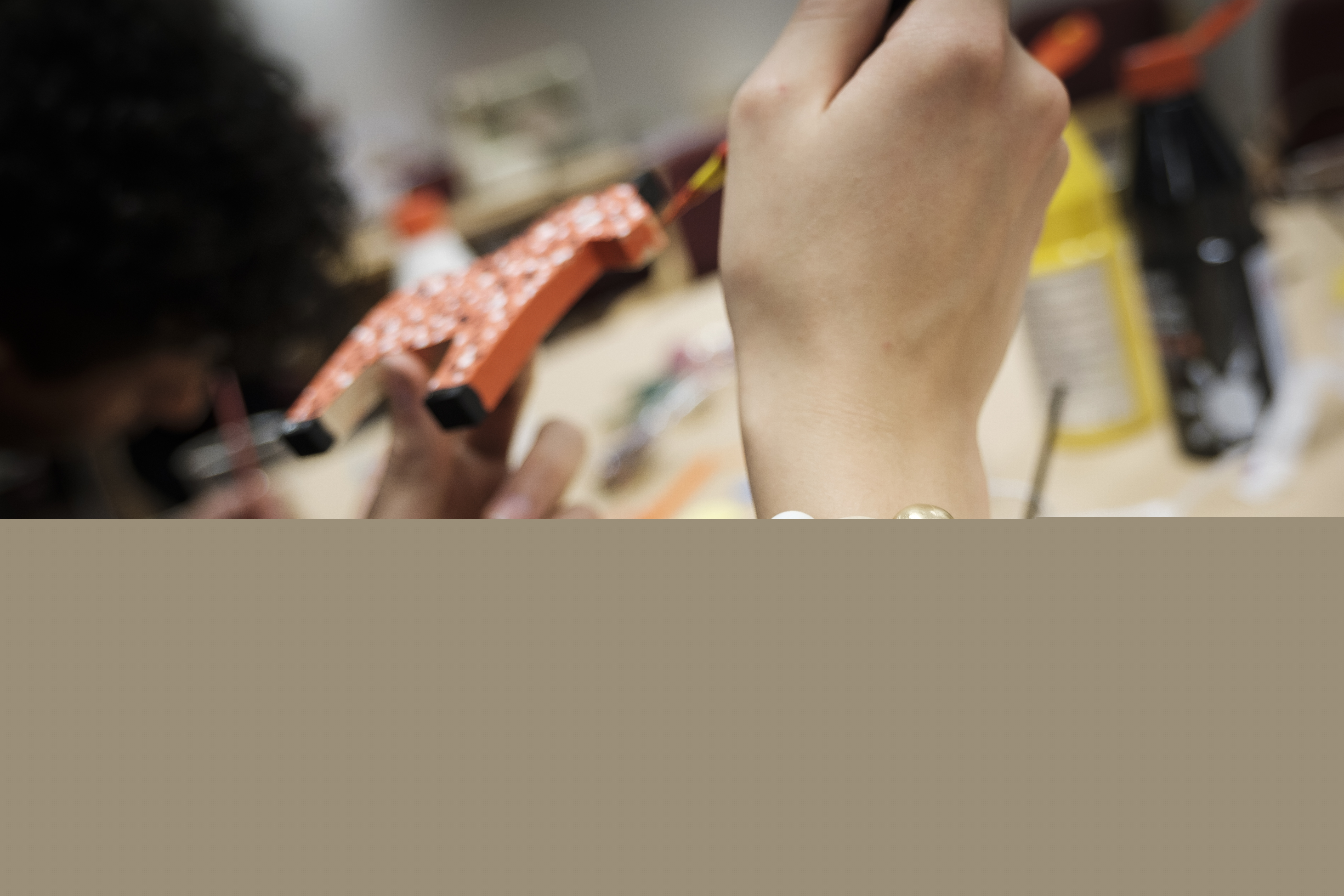 En person med ett korsarmband målar en liten trähäst.