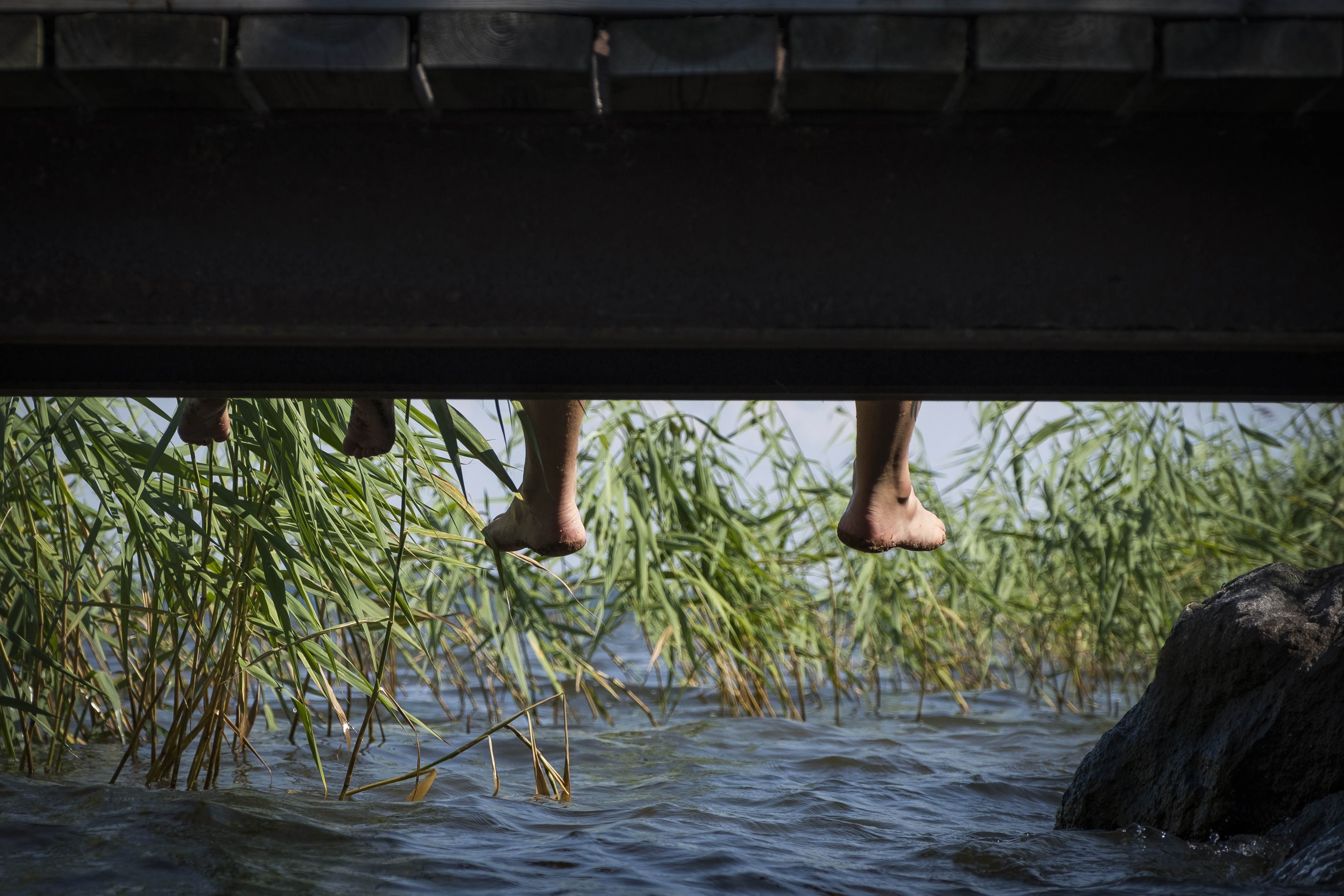 Några ben dinglar över vattnet från en brygga.