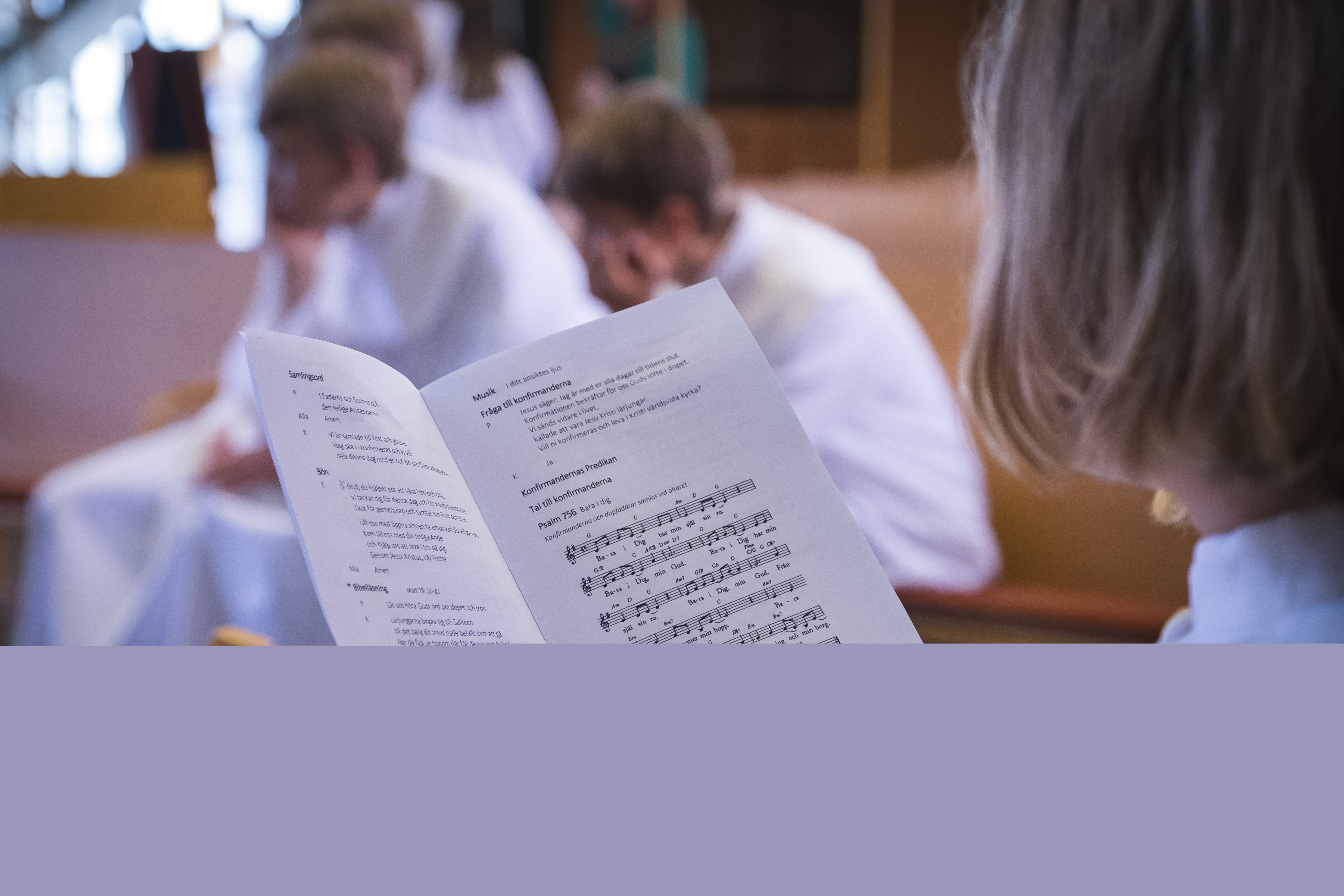 En konfirmand läser i ett sånghäfte. Fler konfirmander sitter i bakgrunden.