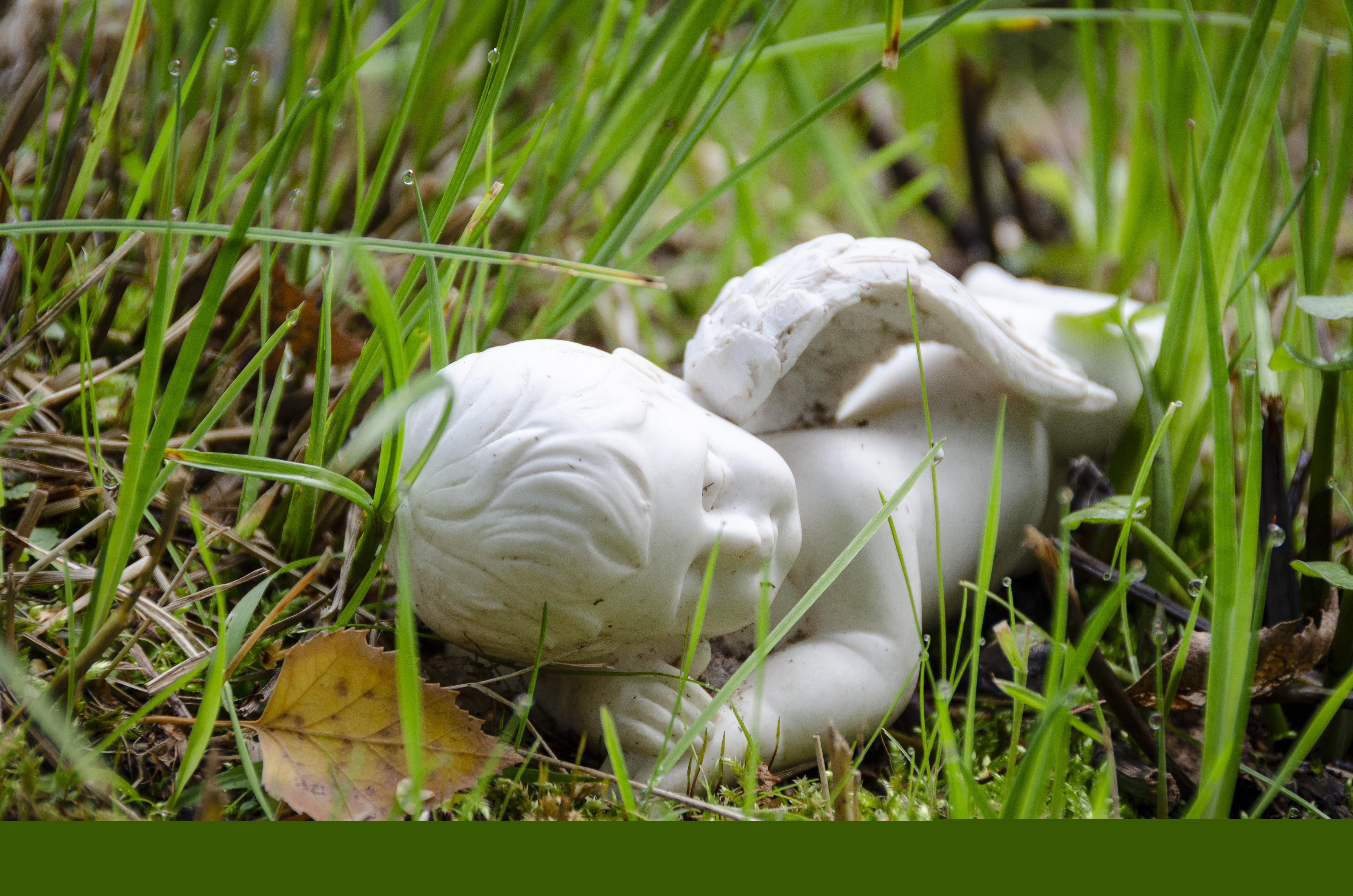 En liten vit stenängel ligger i gräset.