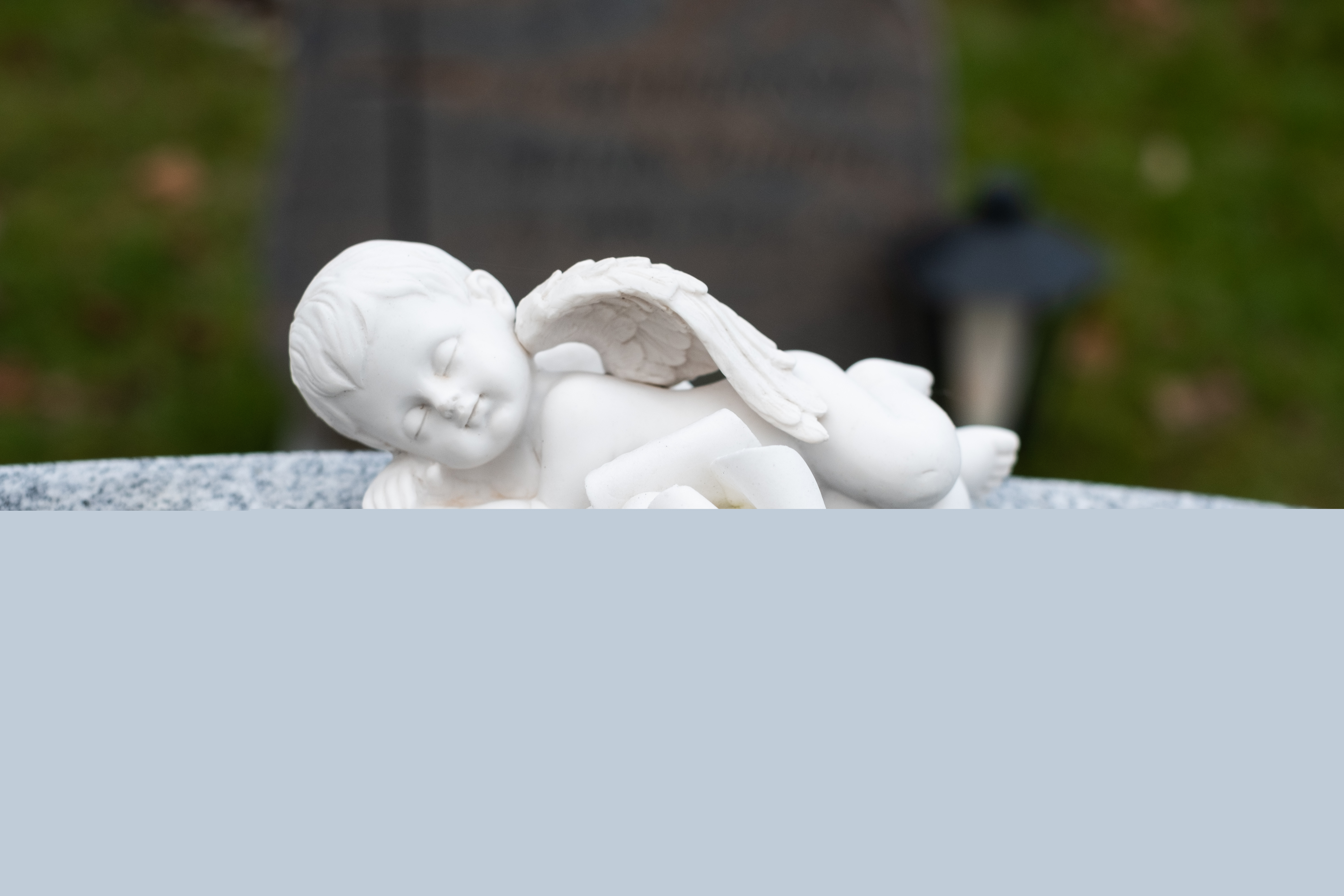 En liten sovande ängel i porslin ligger på en gravsten.