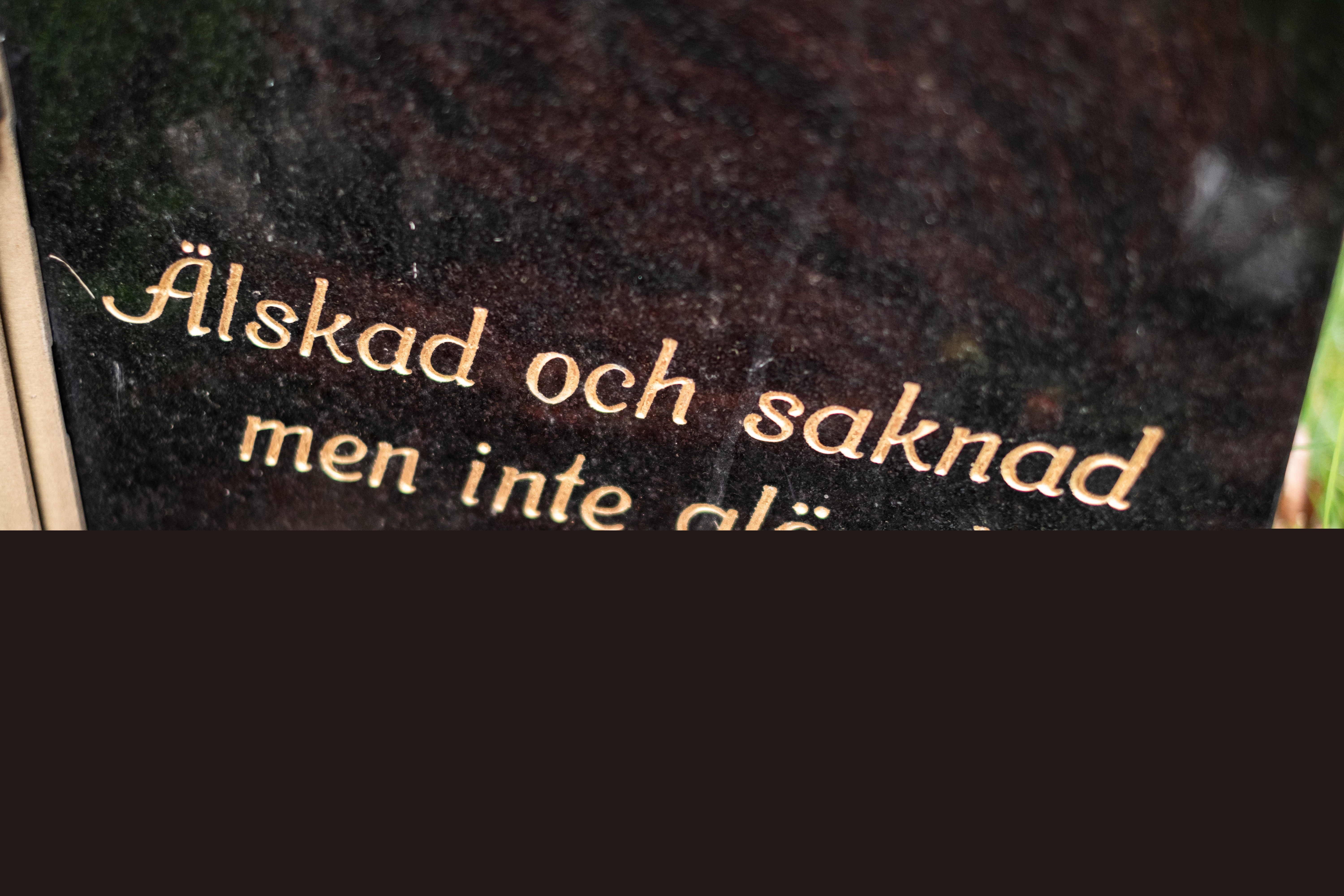 En svart gravsten med guldfärgad text: Älskad och saknad men inte glömd.