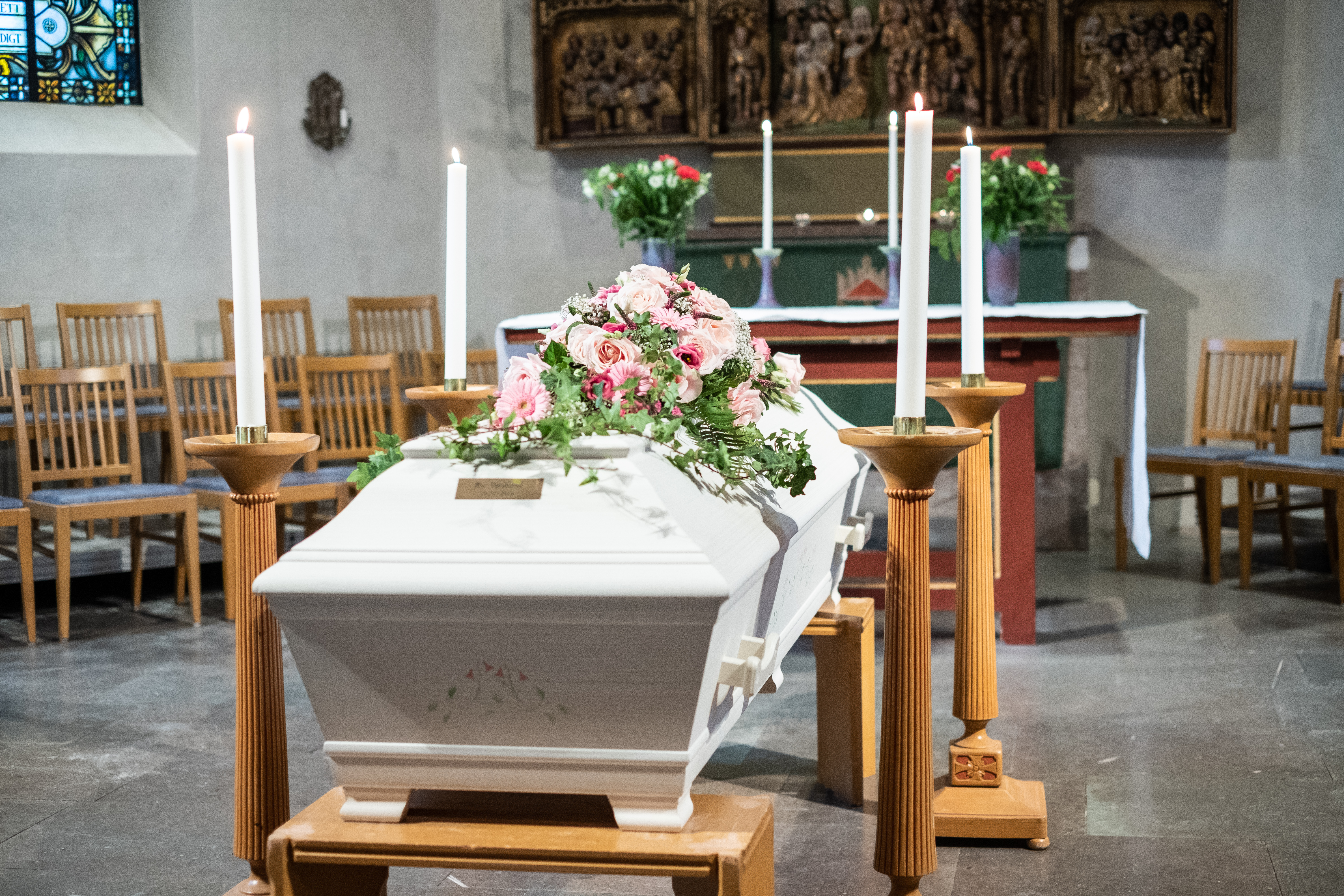 En vit kista med ljusrosa blommor står i ett kor.