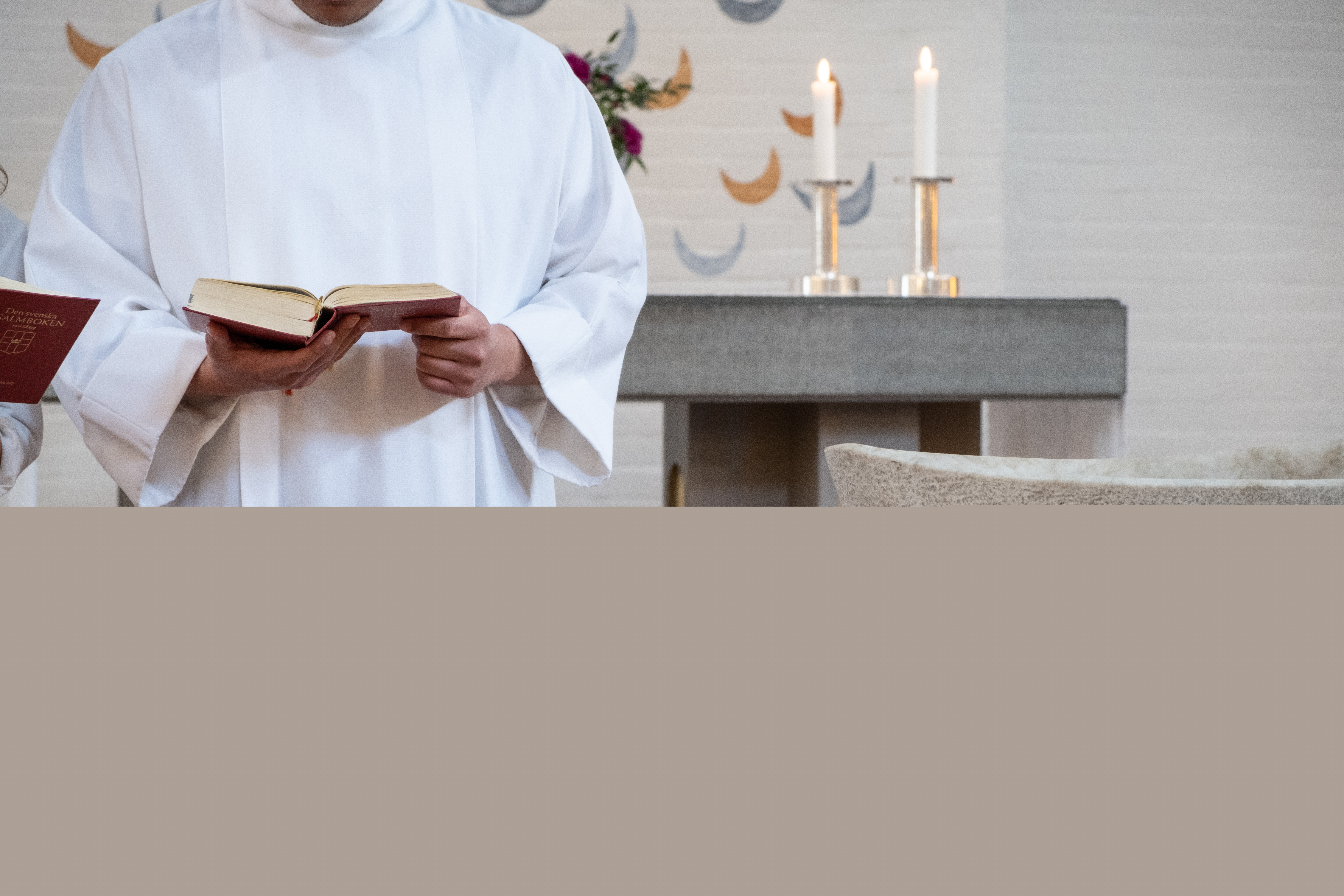 En man i vit kåpa står vid en dopfunt.