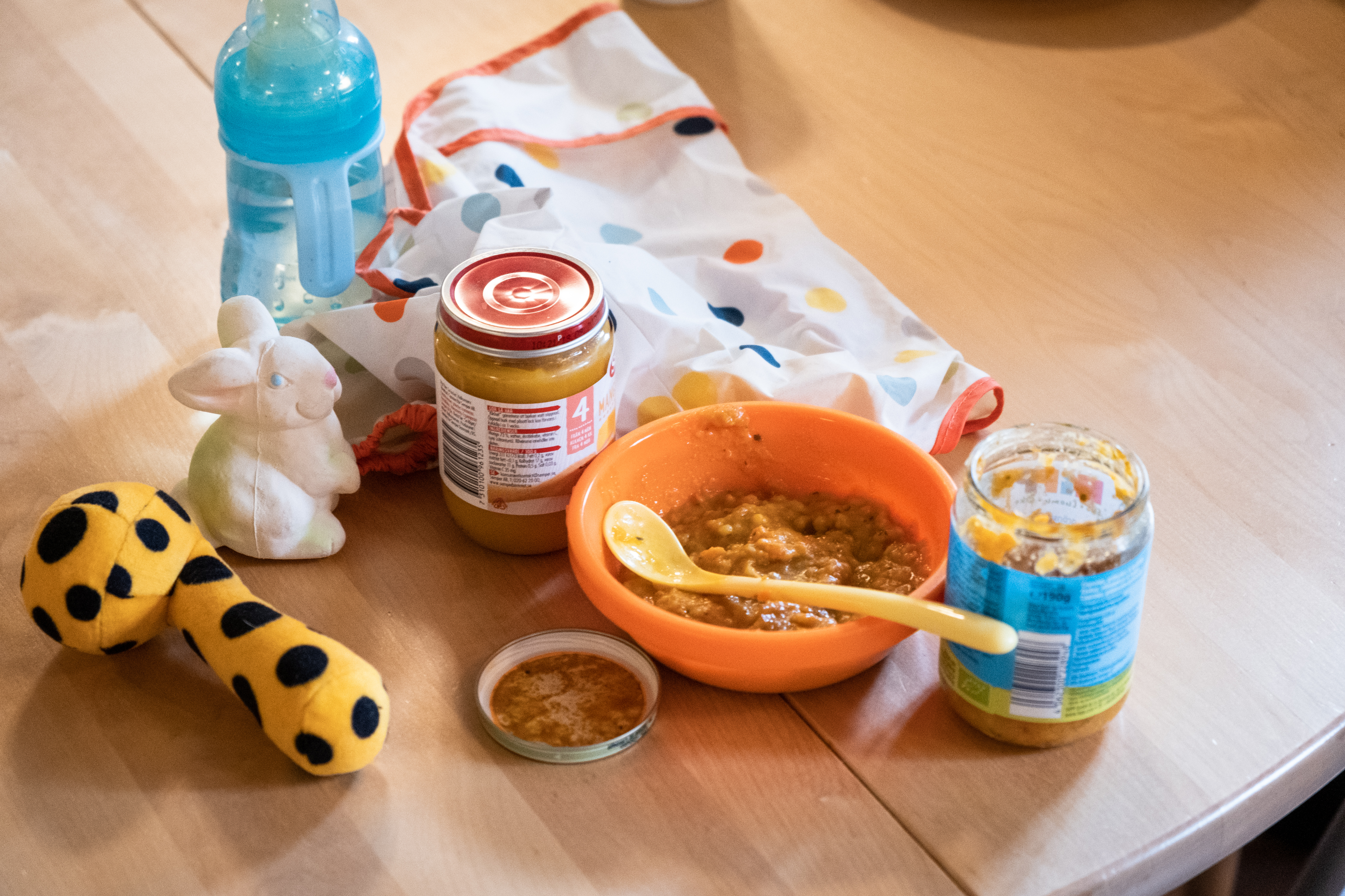 Barnmat, en nappflaska och några leksaker ligger på ett bord.