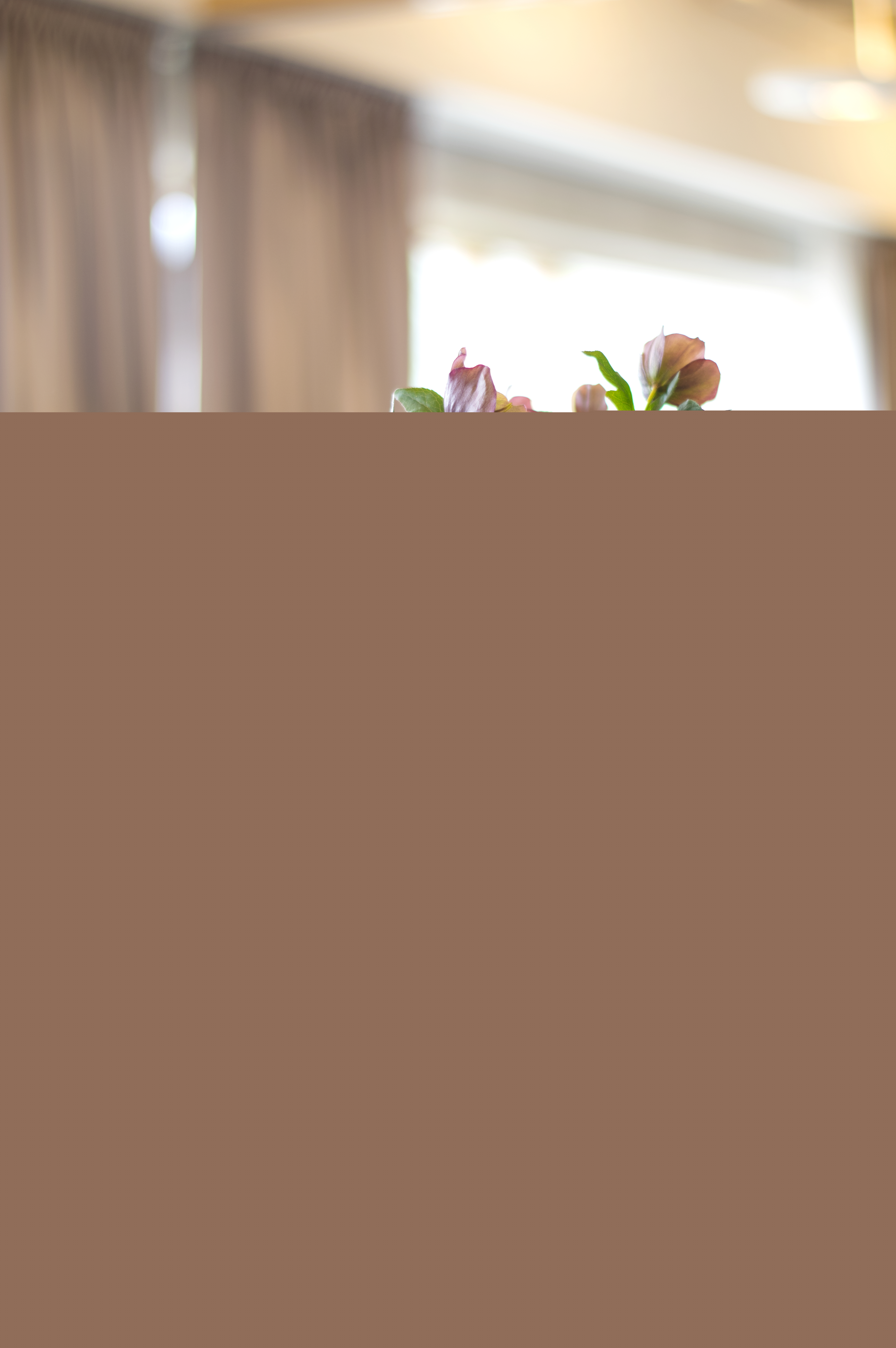 En rosa blombukett står i en vas på ett bord med några tallrikar och bestick.