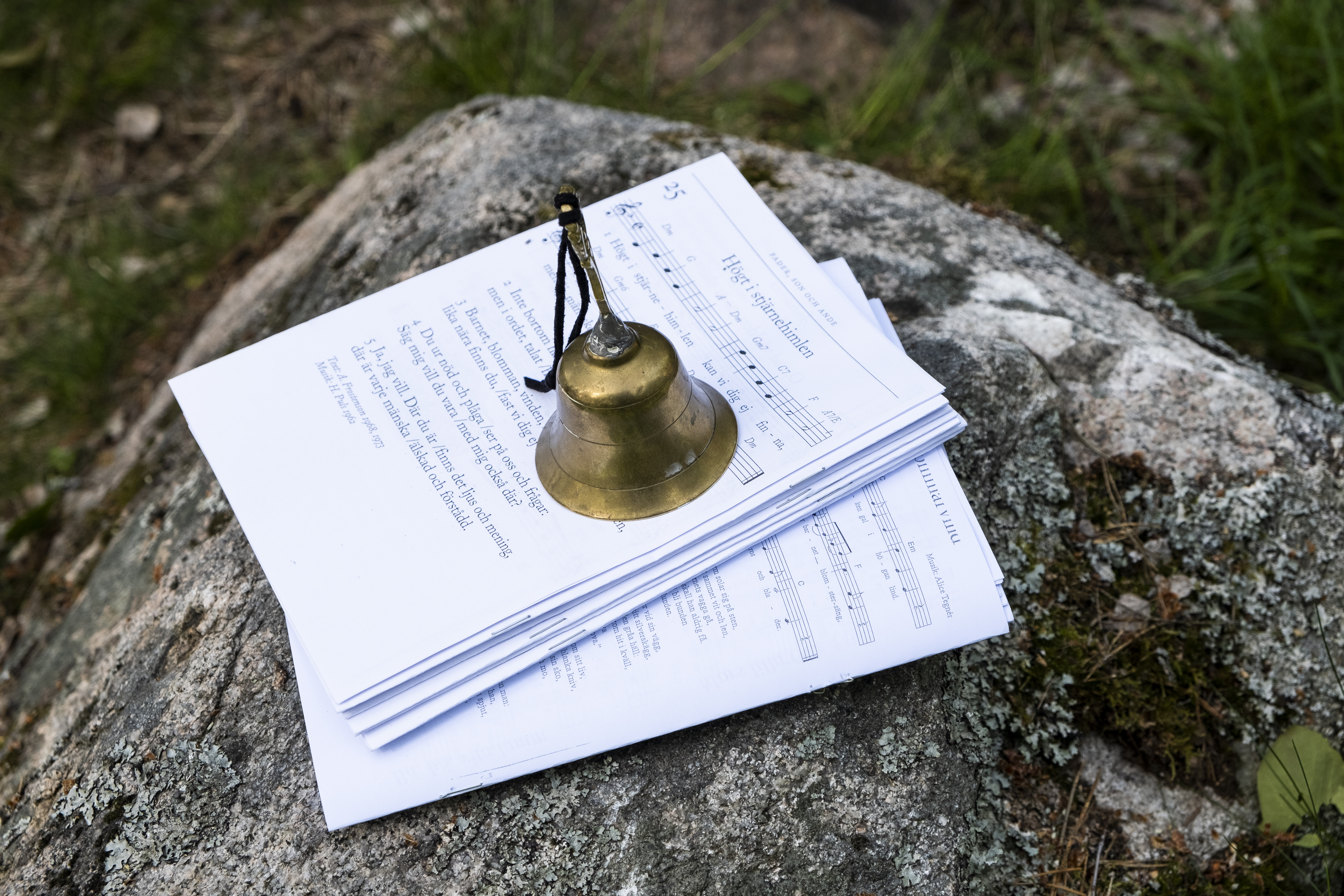 På en sten ligger notpapper. En ringklocka står ovanpå så de inte blåser iväg.