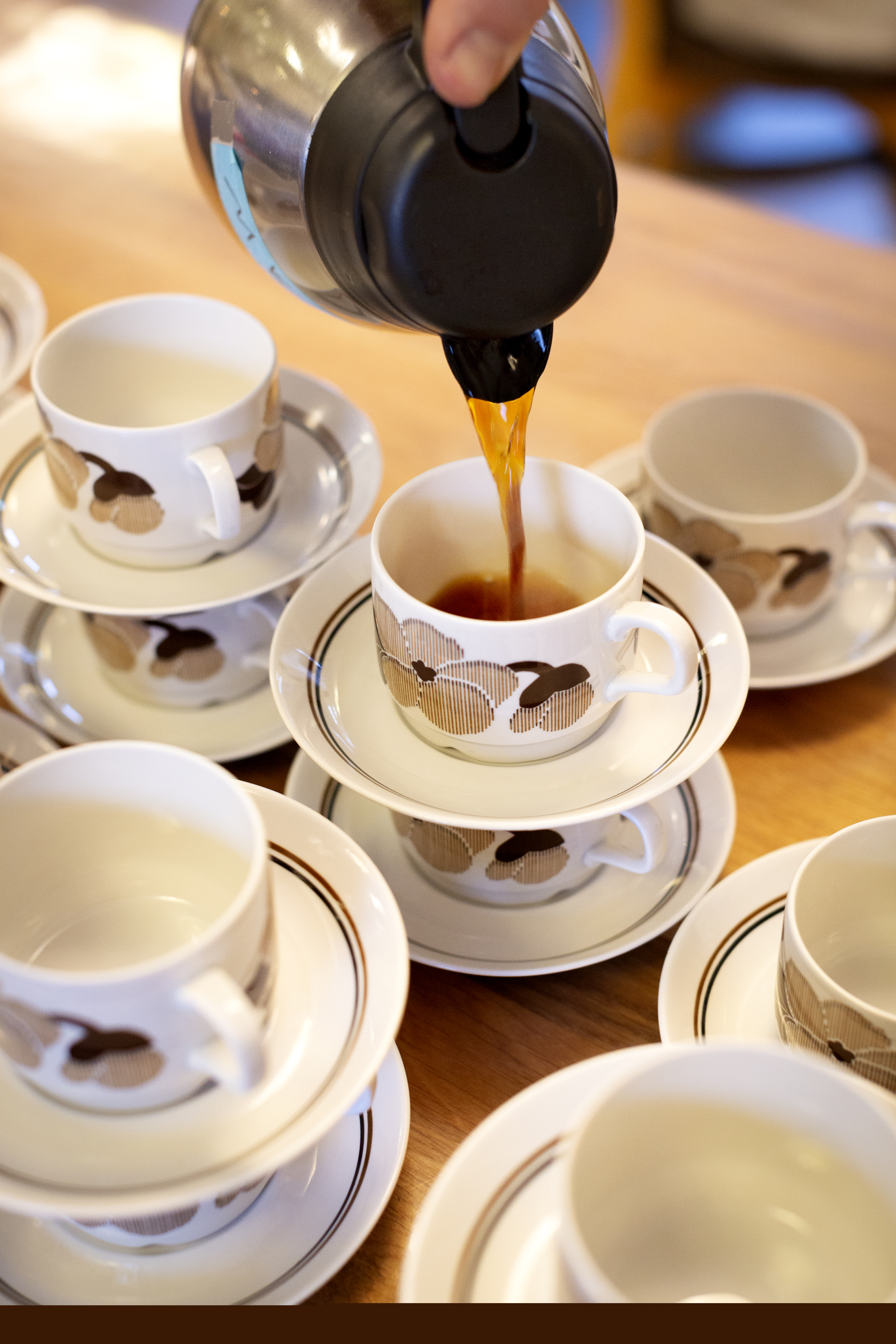 Någon häller upp kaffe i en av flera kaffekoppar som dukats fram på ett bord.