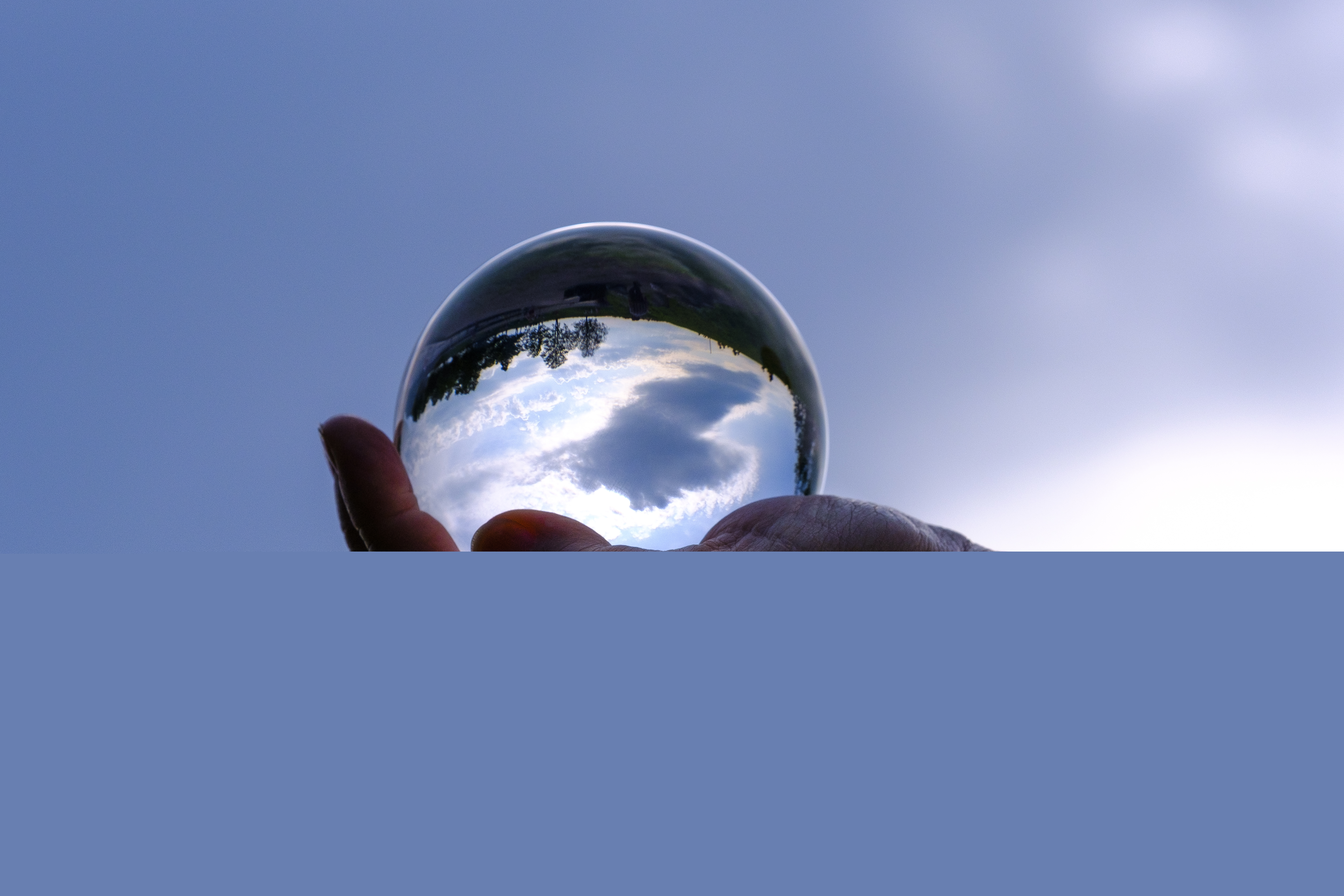 En kupad hand håller ett glasklot. Blå himmel i bakgrunden.