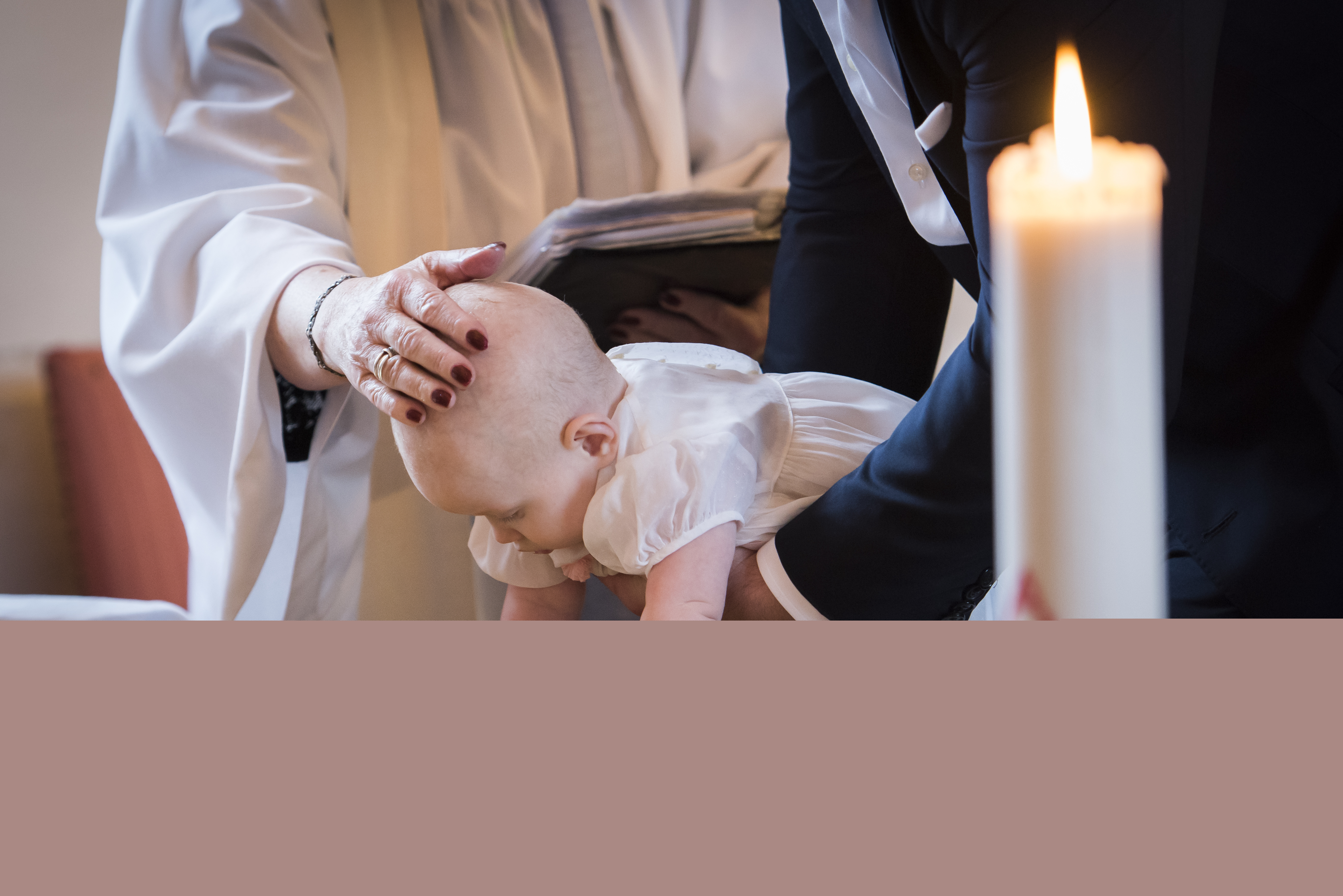 Någon sänker en bebis ner i dopfunten medan prästen håller sin hand på barnets huvud.