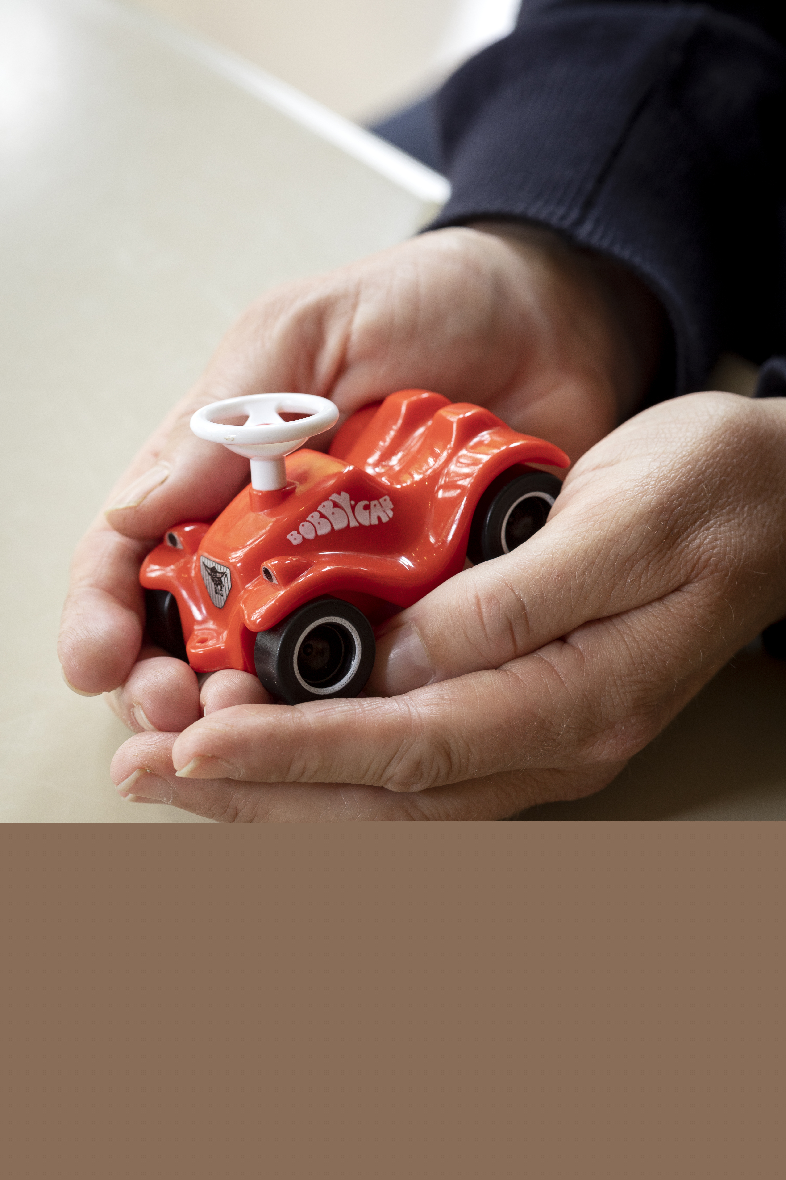 Ett par händer kupade runt en miniatyr av en röd Bobbycar.